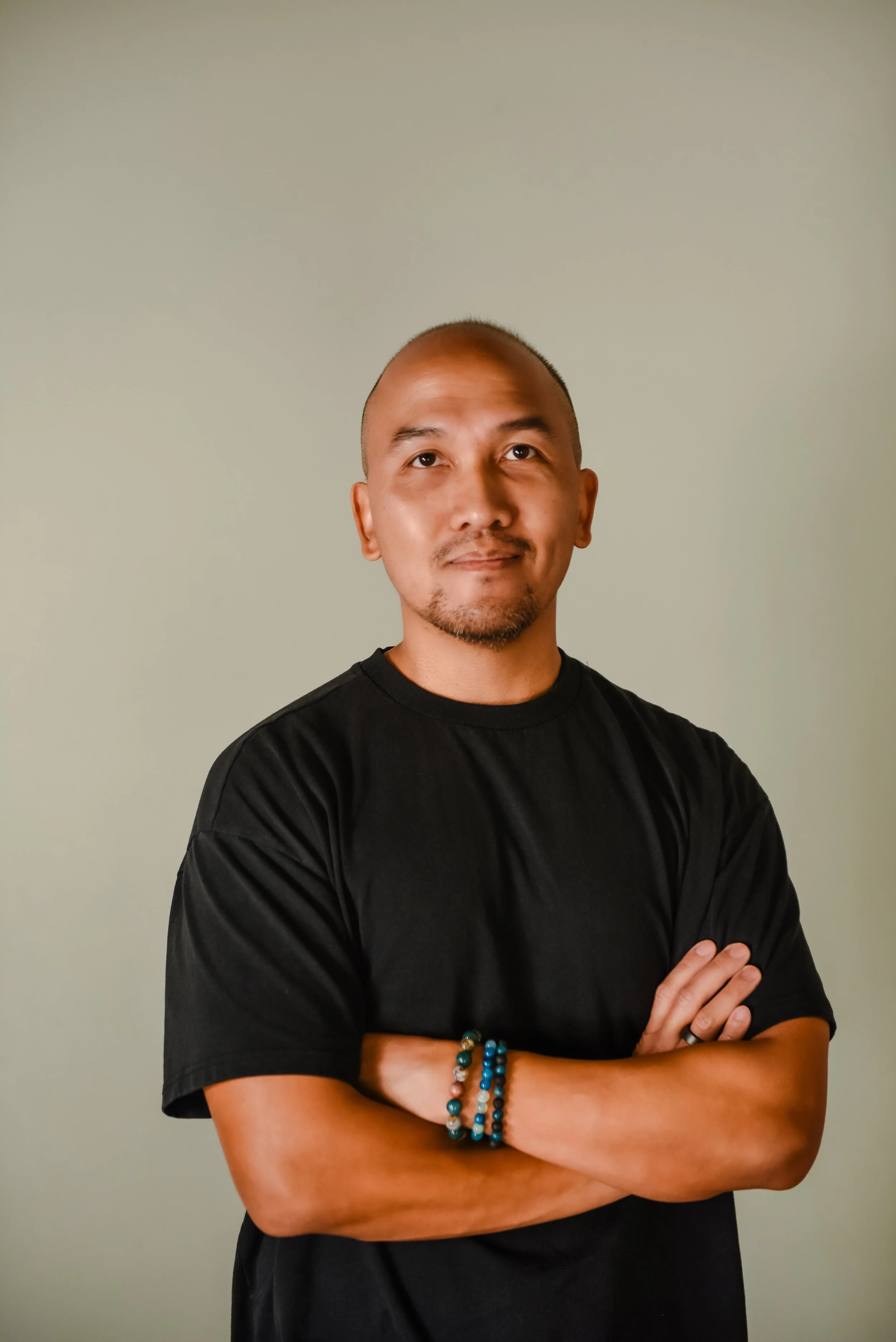 Close-up of a smiling man with a shaved head and goatee, wearing a purple shirt, against a plain light background.