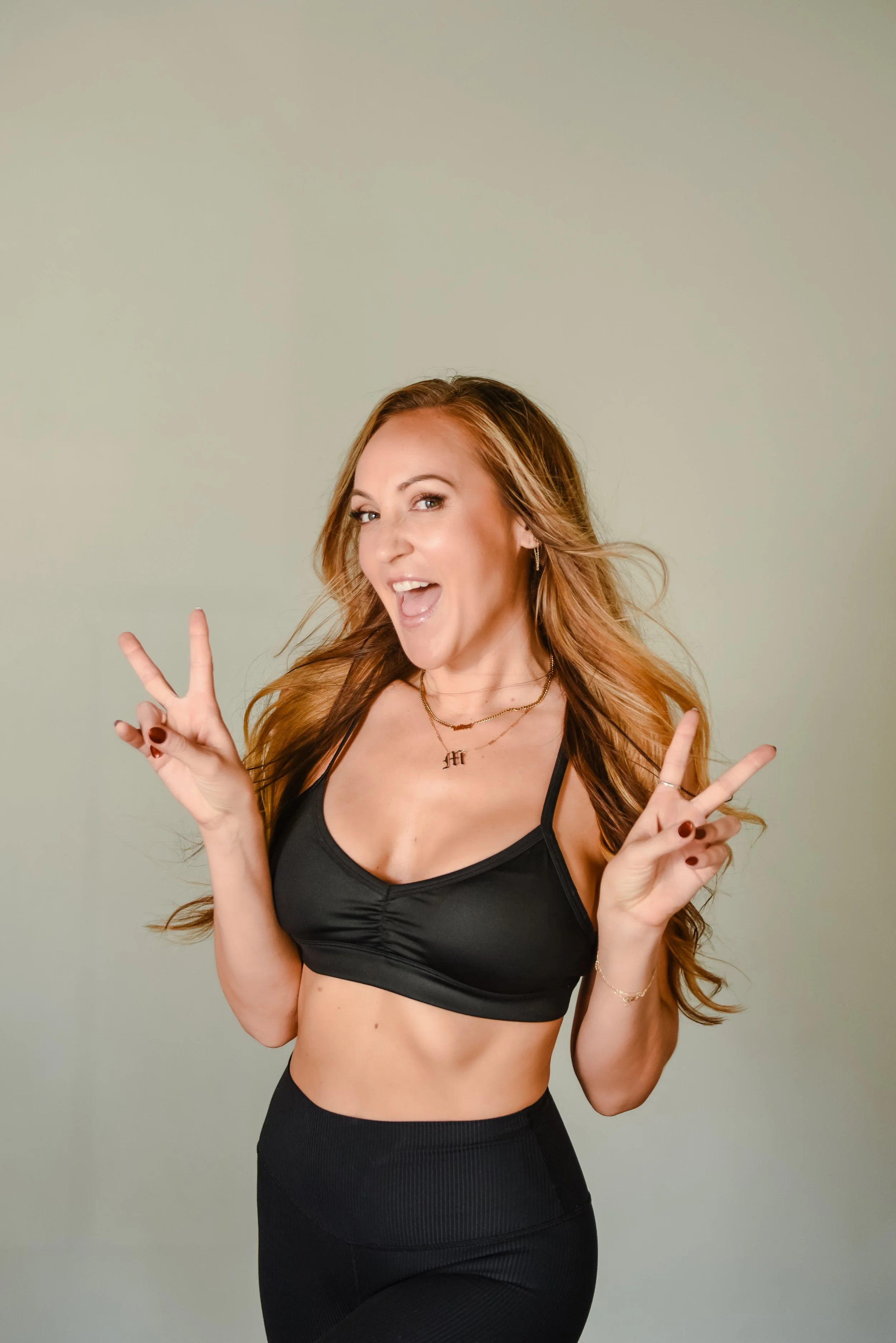 A woman with long blonde hair and a black top smiling against a stone wall background.