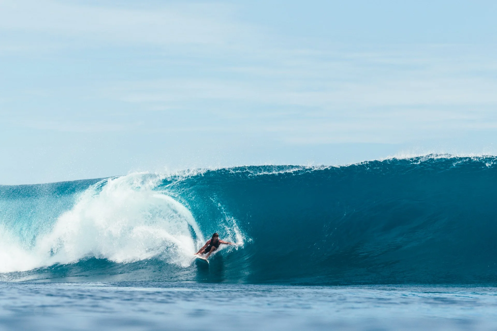 A person surfing on a large ocean wave under a cloudy sky.