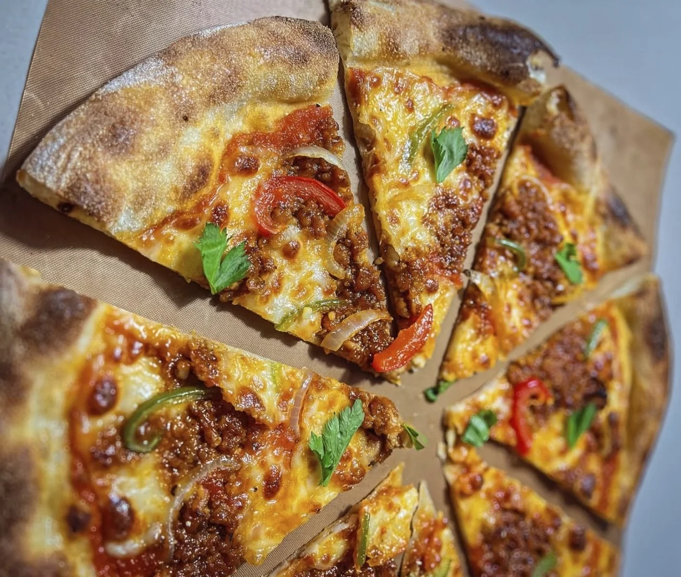 Slices of cheeseburger pizza with ground beef, sliced peppers, onions, melted cheese, and garnished with fresh cilantro leaves.