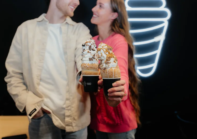 A couple holding Crispy Cones in front of a neon cone sign