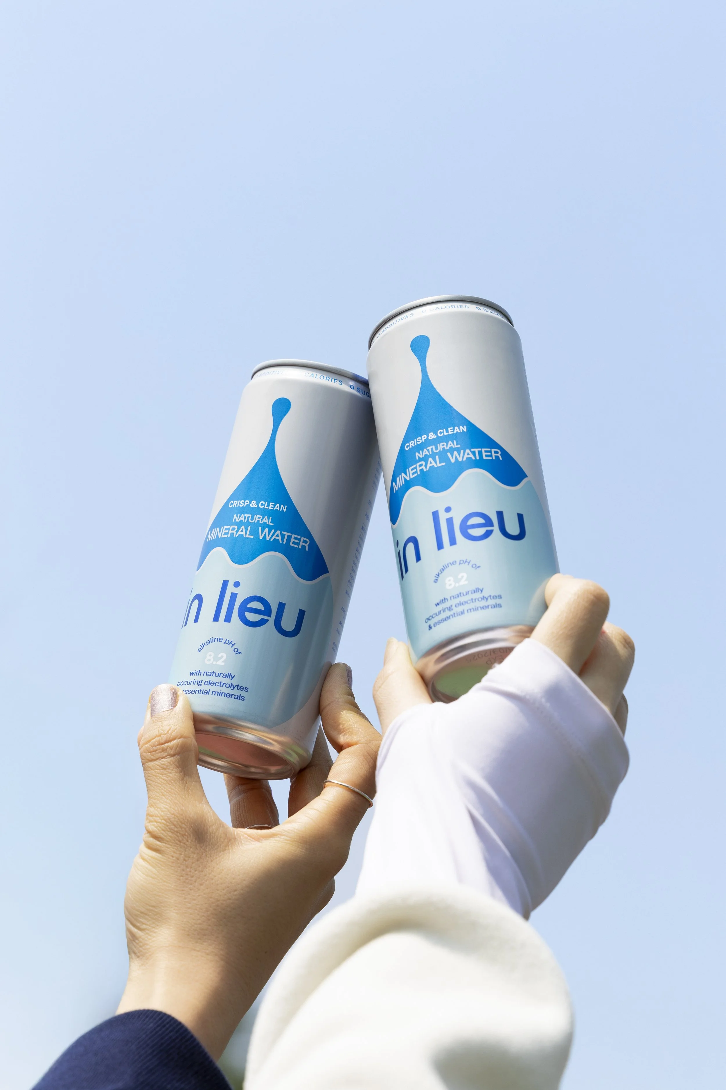 Two cans of mineral water being held up against a clear blue sky.