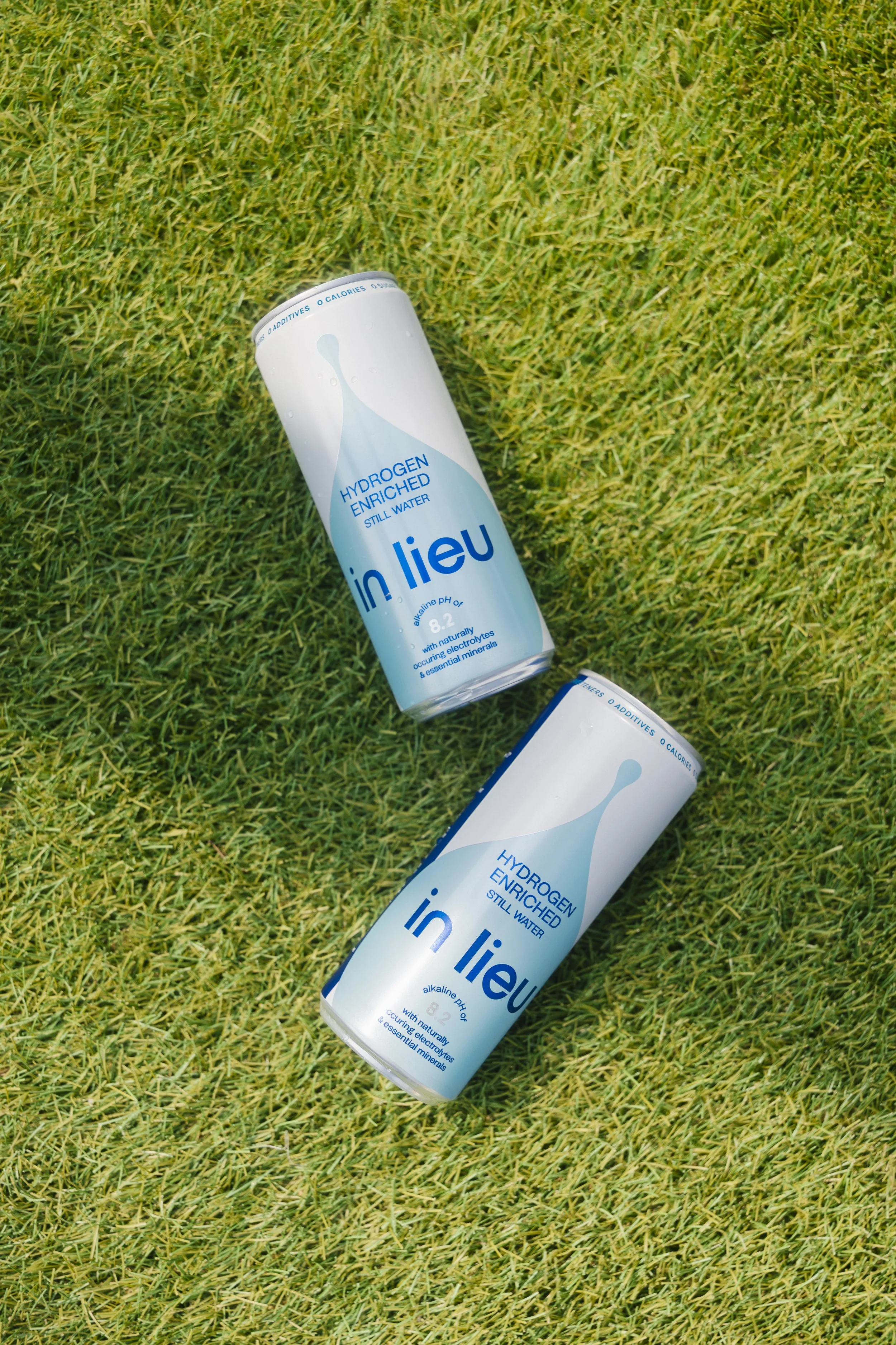 Two cans of in lieu hydrogen-enriched still water lying on green grass.