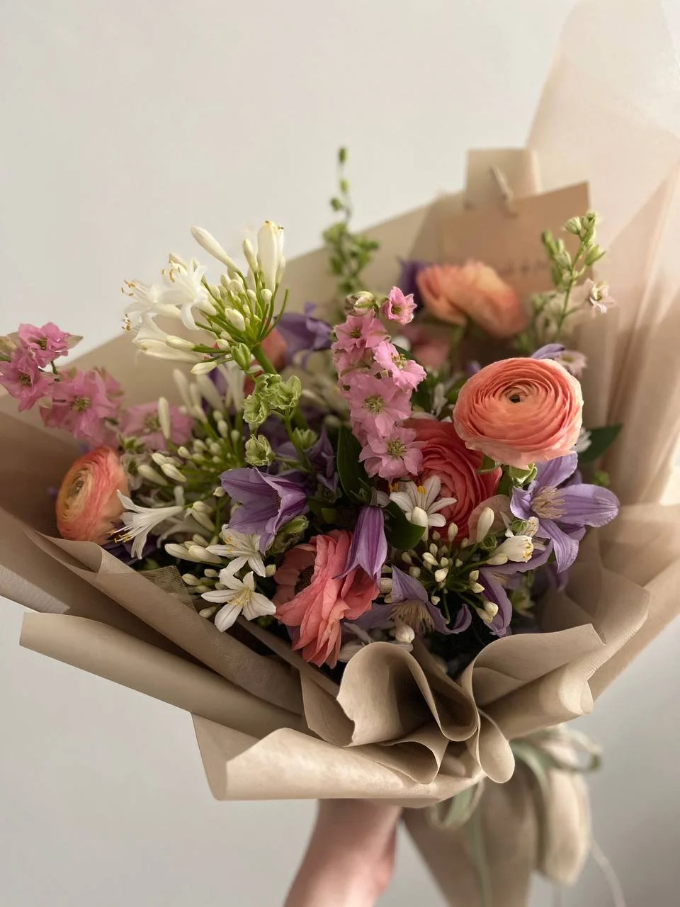 Bouquet of pink, purple, white, and green flowers wrapped in beige paper