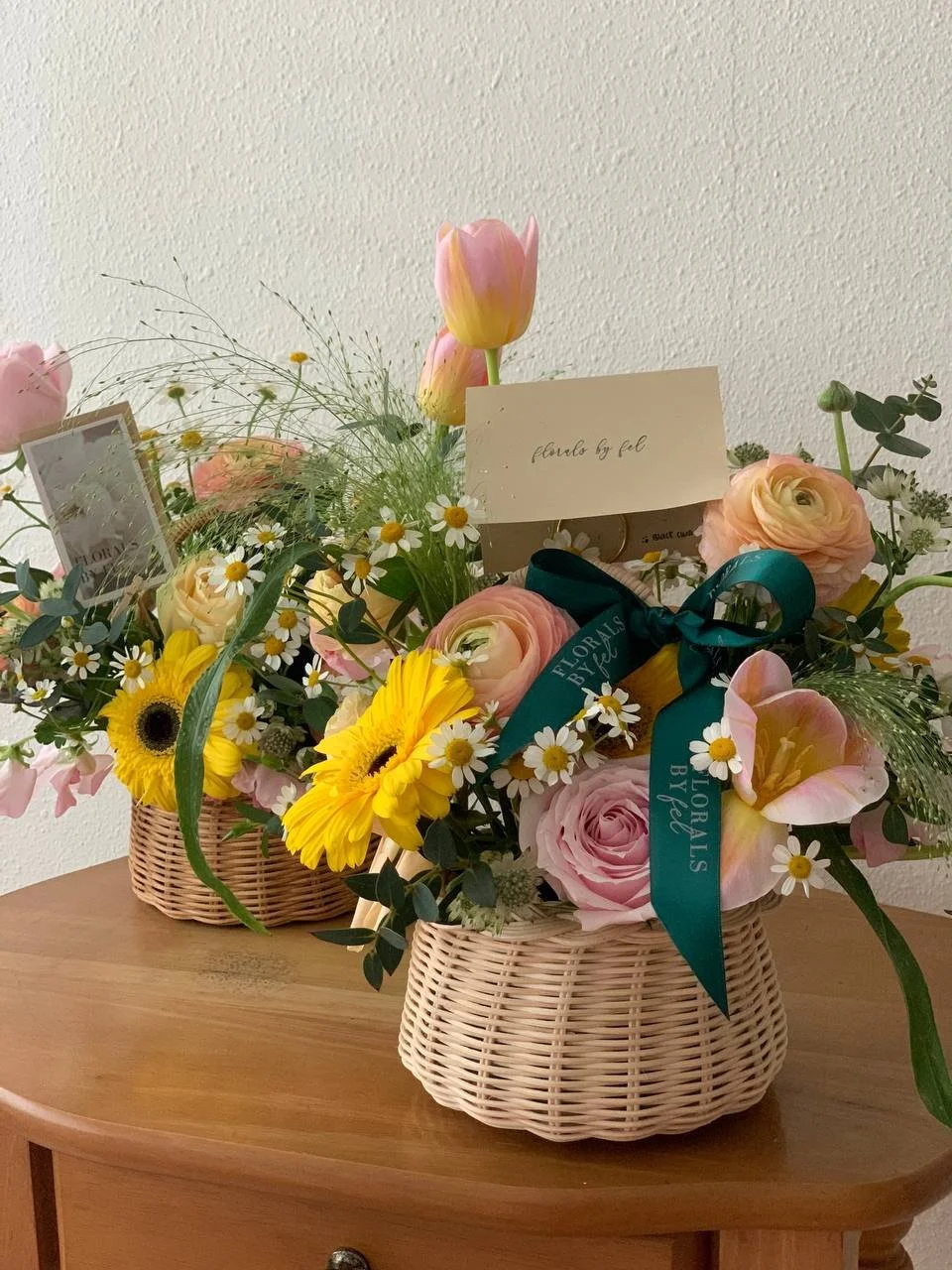 Two baskets with pink, yellow, and white flowers on a wooden table.