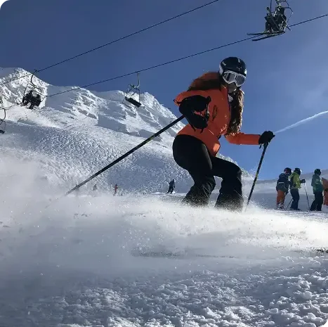 A woman skiing on snow at a ski resort, with a ski lift and other skiers in the background.