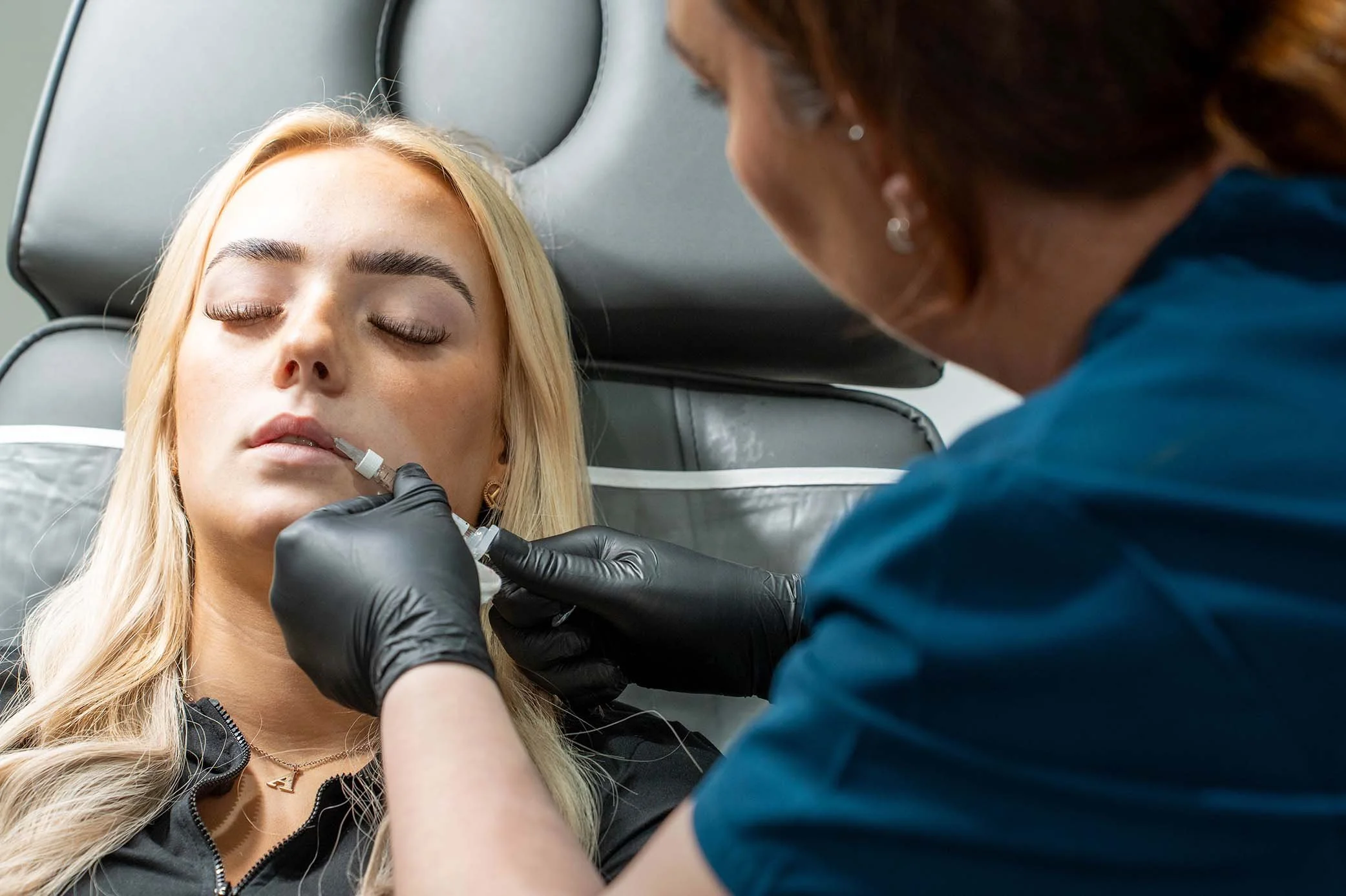 A medical aesthetician performing a lip filler procedure on a customer.