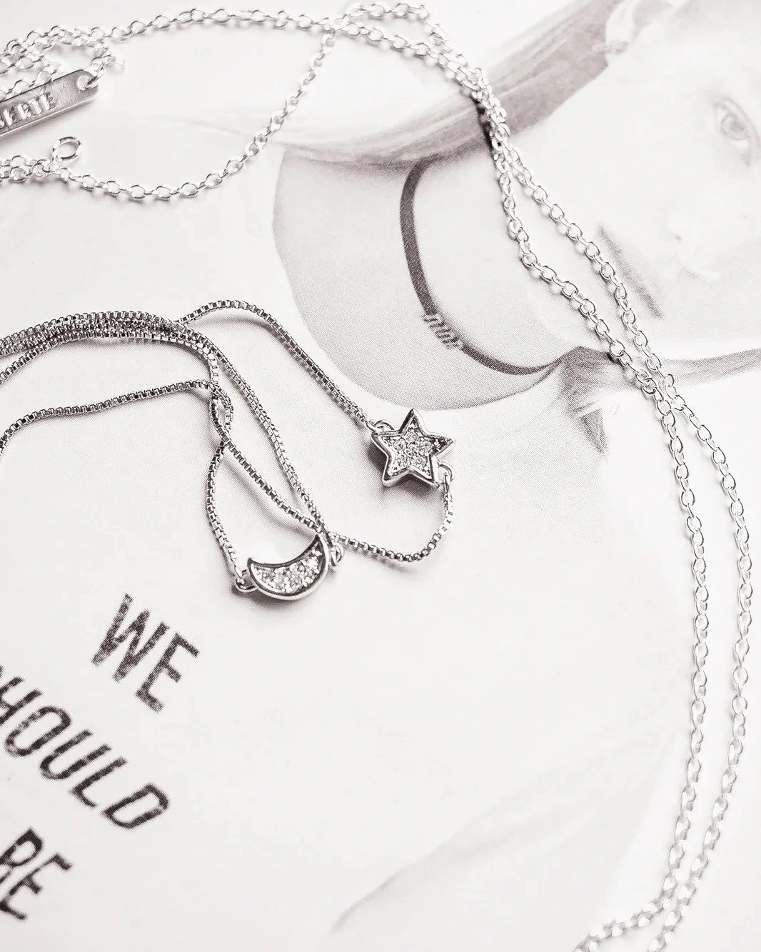 Silver jewelry including necklaces with star and moon pendants resting on a magazine featuring a woman's face.