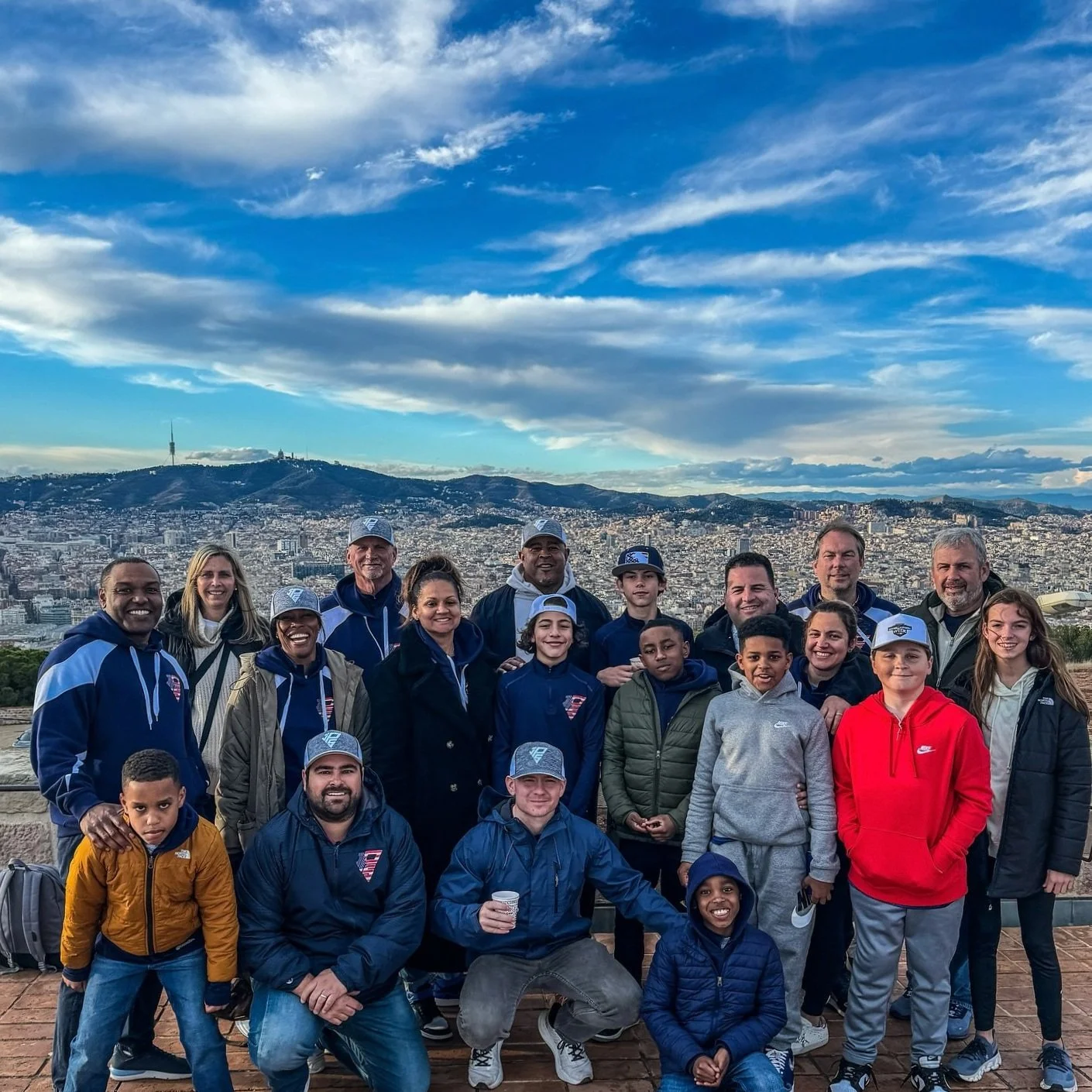 Group of people posing outdoors with a cityscape and mountains in the background under a blue sky.