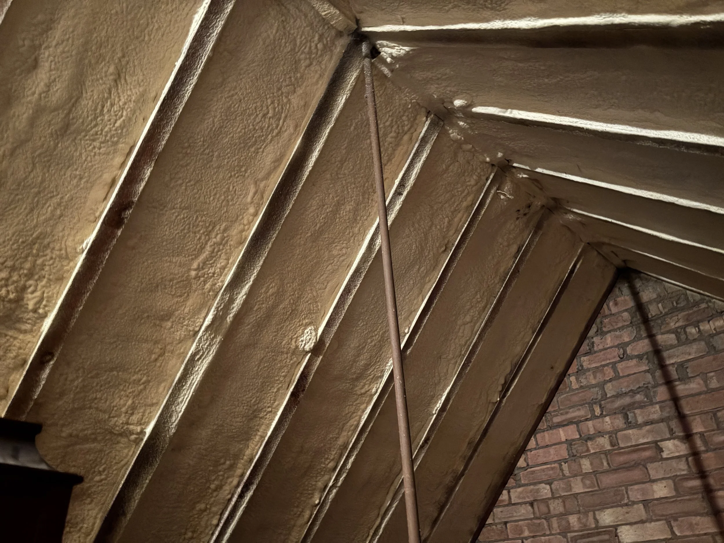 Close-up view of a textured cornice or ceiling molding with a metallic inspection tool or rod extending toward the corner of a room. The room features beige textured walls and a brick wall. The image is taken at an upward angle, focusing on the junction between the walls and ceiling.