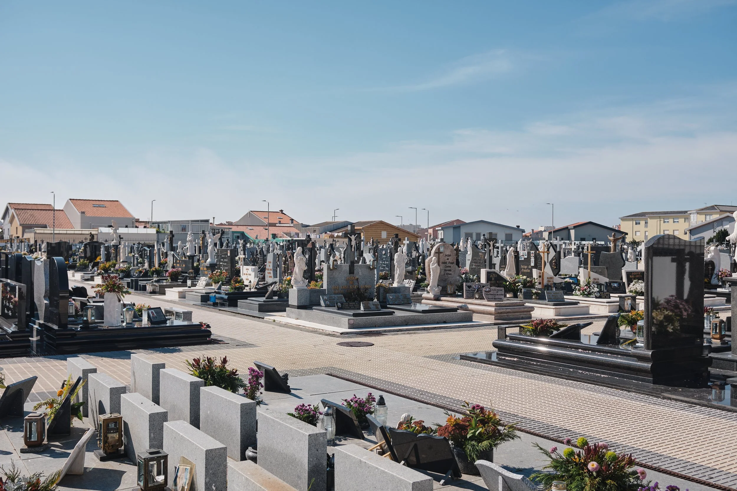 A cemetery with numerous graves, headstones, and flowers under a clear blue sky.