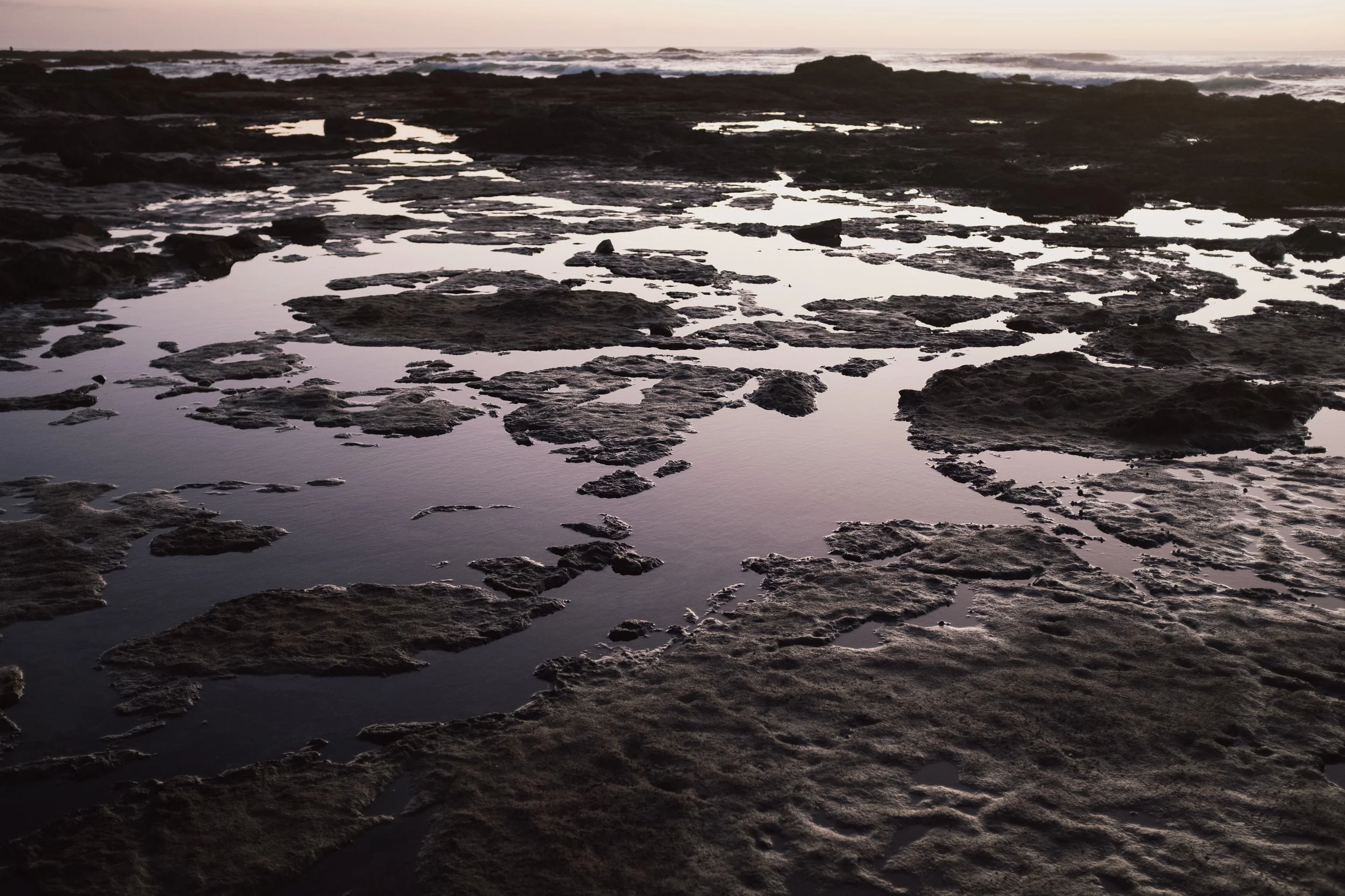 Rocky shoreline at sunset with tide pools and reflections in the shallow water.