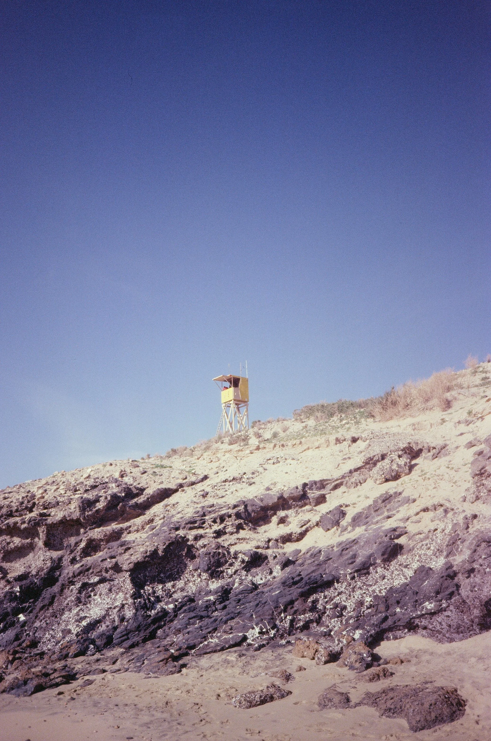 A lifeguard tower on a rocky sandy beach under a clear blue sky