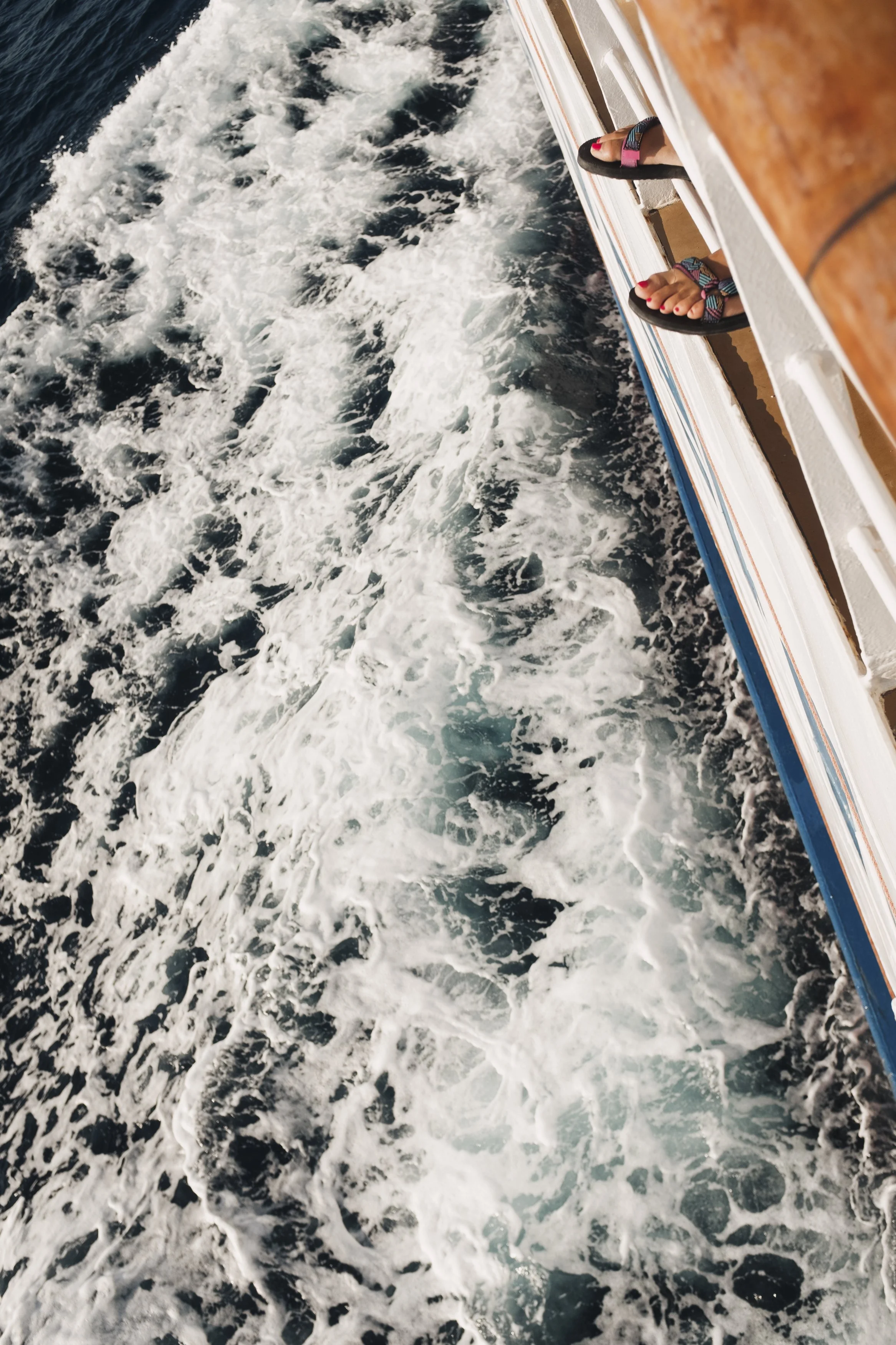 Footwear of two people on a boat deck with a view of the moving water below.