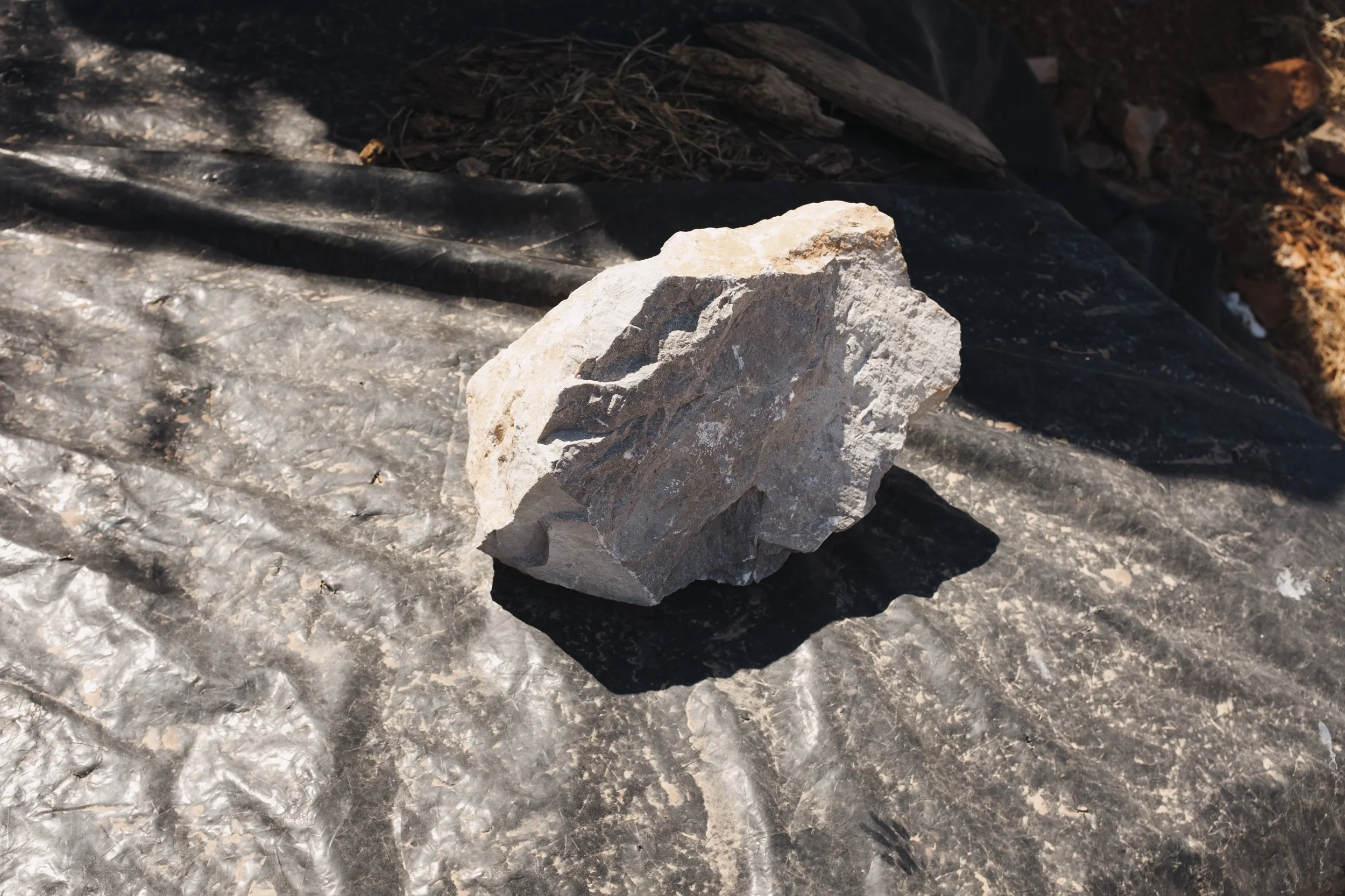 A light-colored, rough rock resting on a black plastic sheet with dirt in the background.