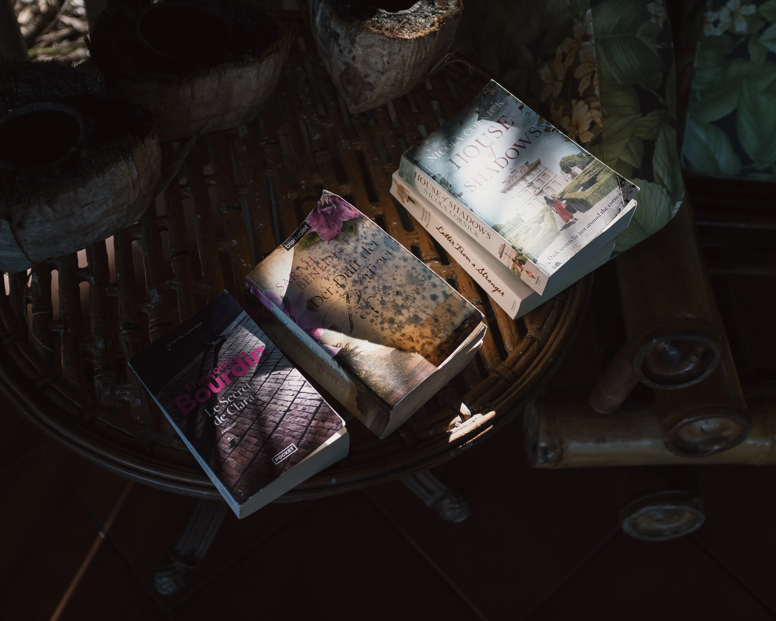 Three books placed on a bamboo table, with a pair of eyeglasses beside them.