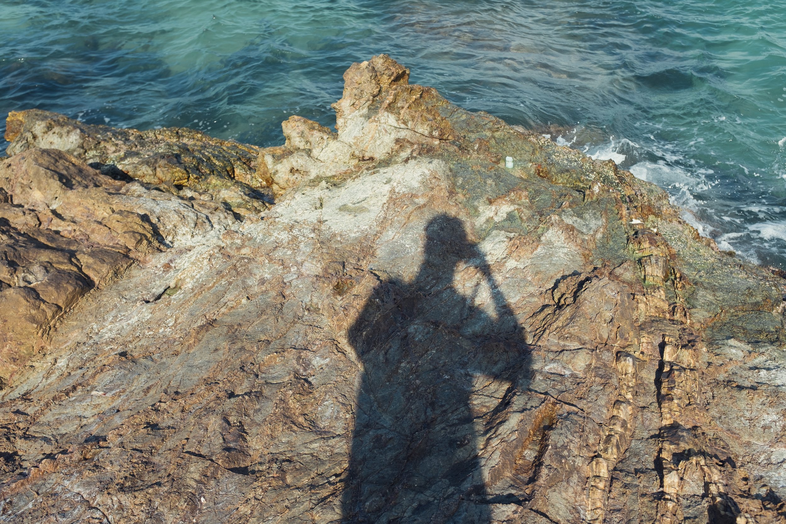 Shadow of a person taking a photo on a rocky shore with the ocean in the background.