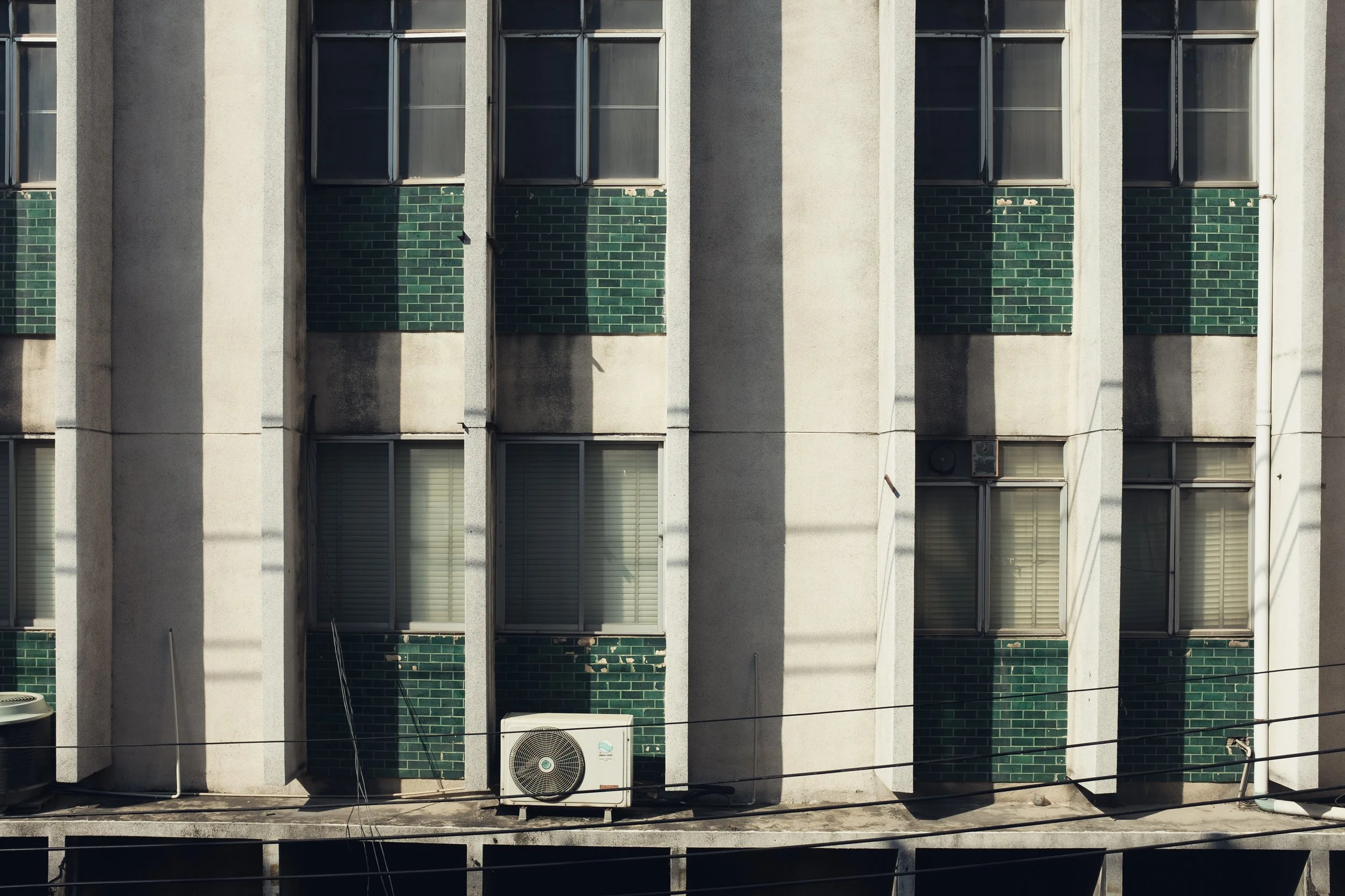 Facade of a multi-story building with vertical columns, windows, and an air conditioning unit outside.