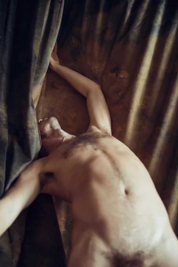 Nude man in front of fabric with one arm extended