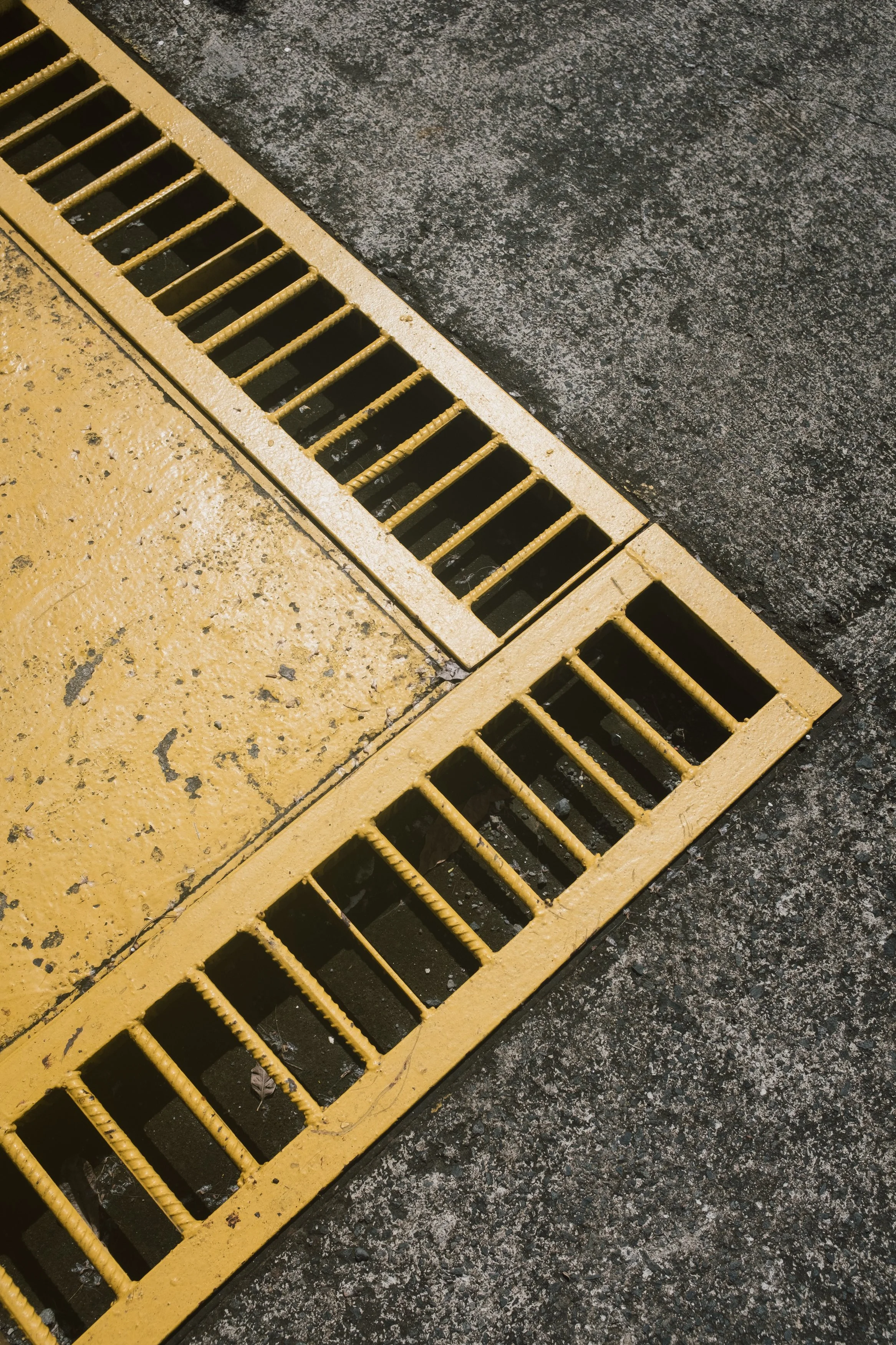 A metal floor drain grate covering a drain, set into the concrete floor, with some dirt and debris visible inside.