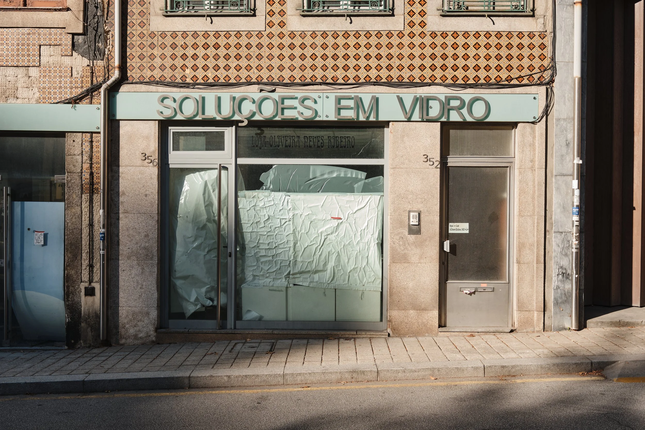 Storefront with the sign 'Soluções em Vidro' and a large window covered with paper, next to a glass door and a metal door.