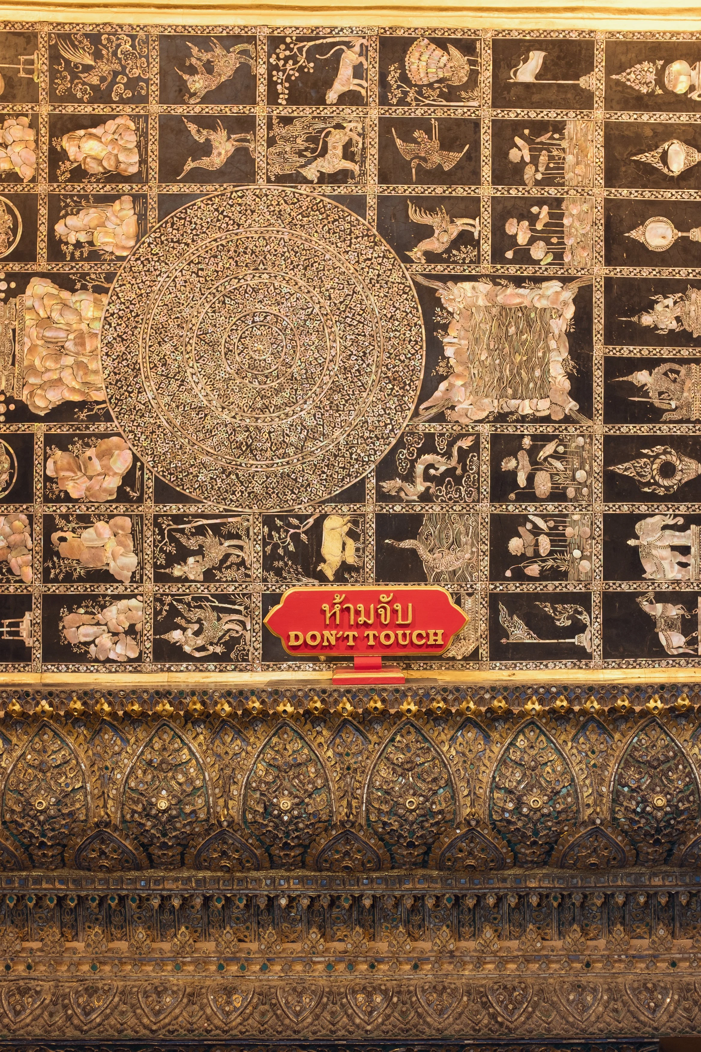 Intricate mosaic depicting various animals and mythological figures with a prominent concentric circle design in the center, located in a temple with a 'Don't Touch' sign in Thai and English.