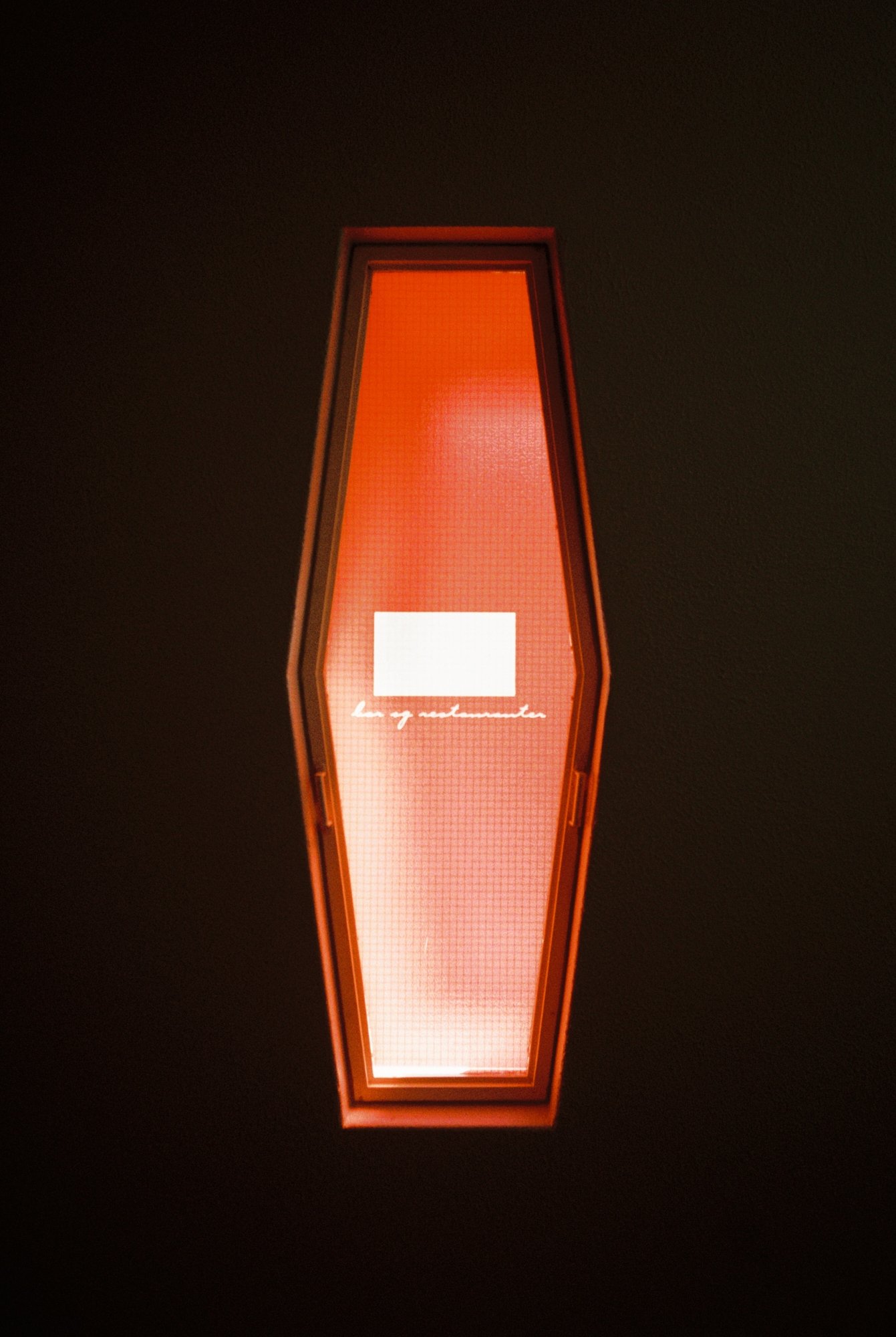 A vertically oriented rectangular illuminated sign with red-orange lighting against a dark background, with white cursive text that reads 'Lagnamenta'.
