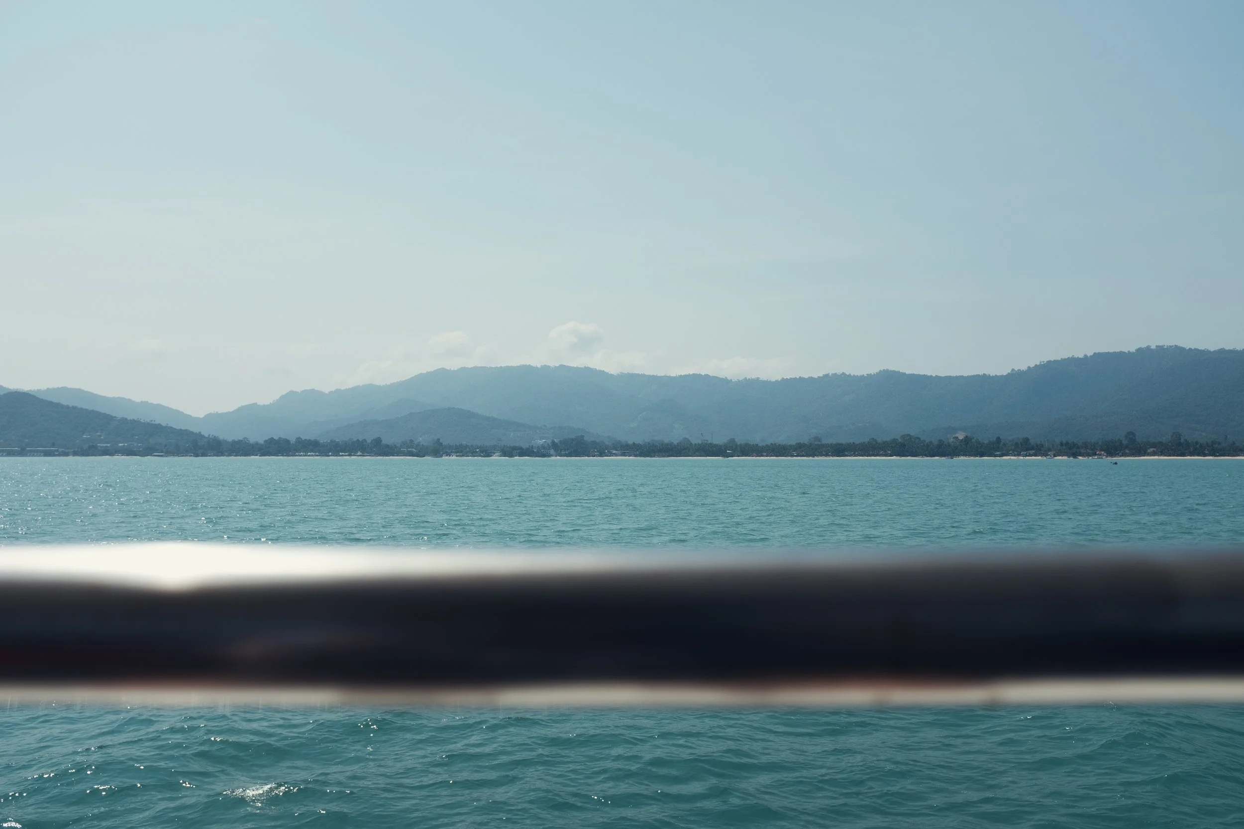 View of a calm ocean with mountains in the distance and a hazy sky above, partially obscured by a horizontal bar in the foreground.