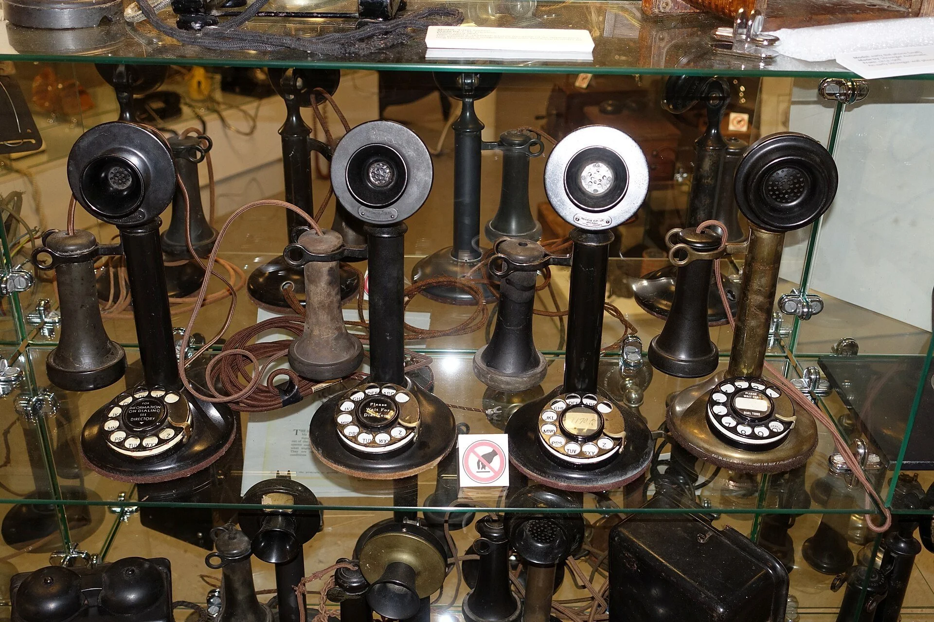 A museum display case of antique candlestick telephones with rotary dials