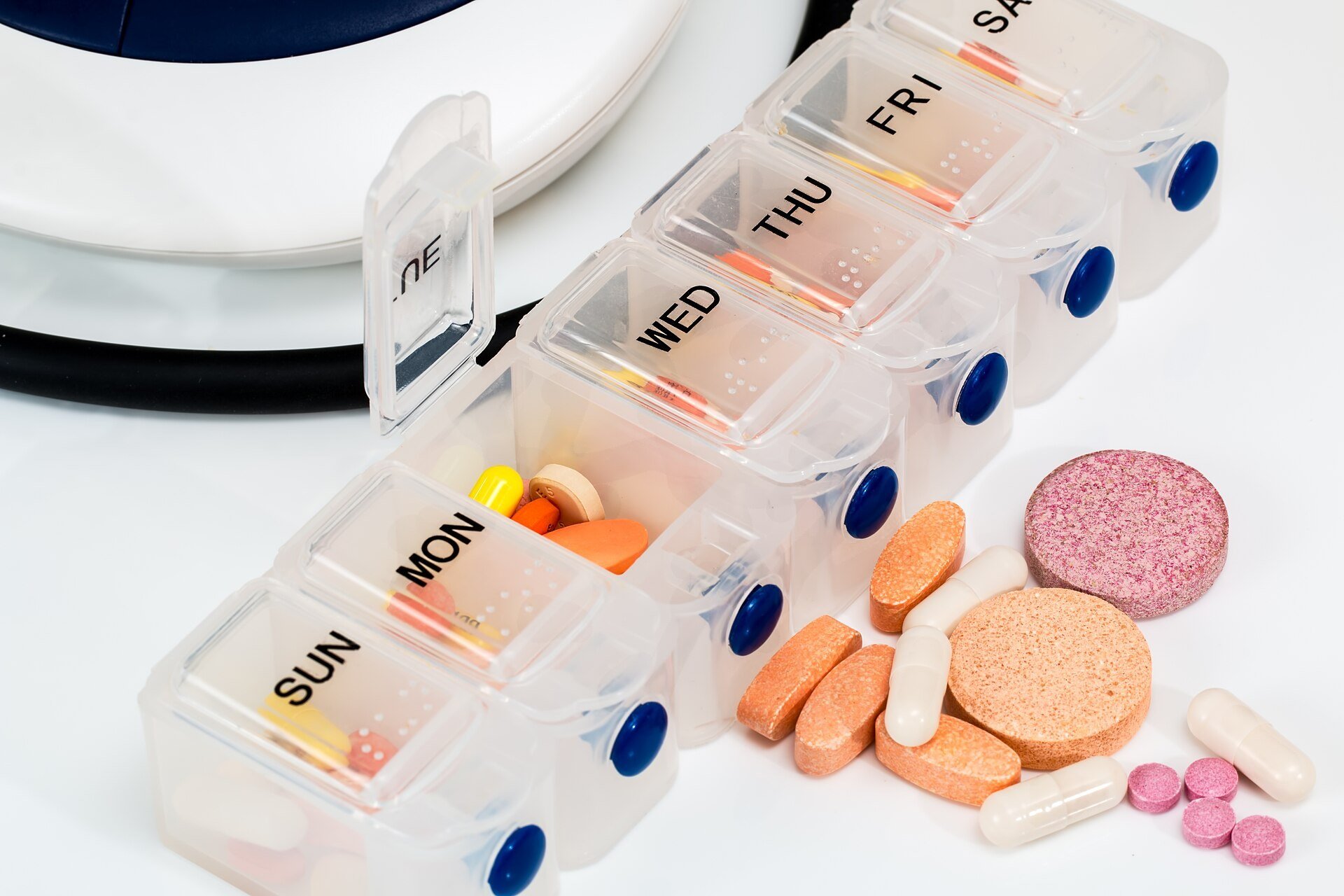 A weekly pill organizer labeled Sunday through Saturday with assorted tablets and capsules beside it