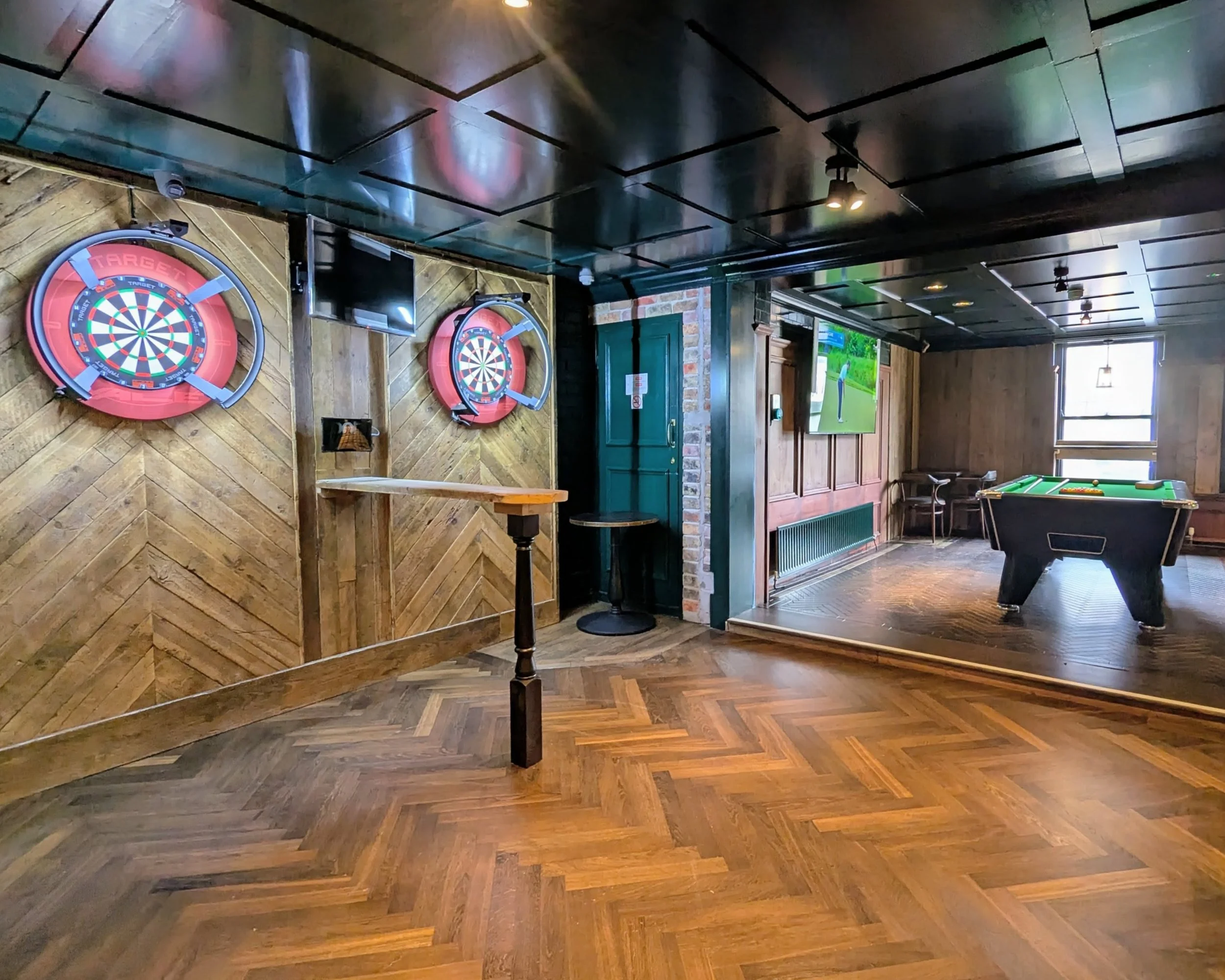 A bar or game room with dartboards on the wall, a pool table, and a television, featuring wooden and brick interior design.