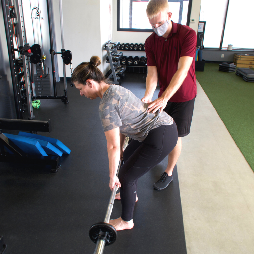 Lynette bending down for deadlit with male trainer providing support