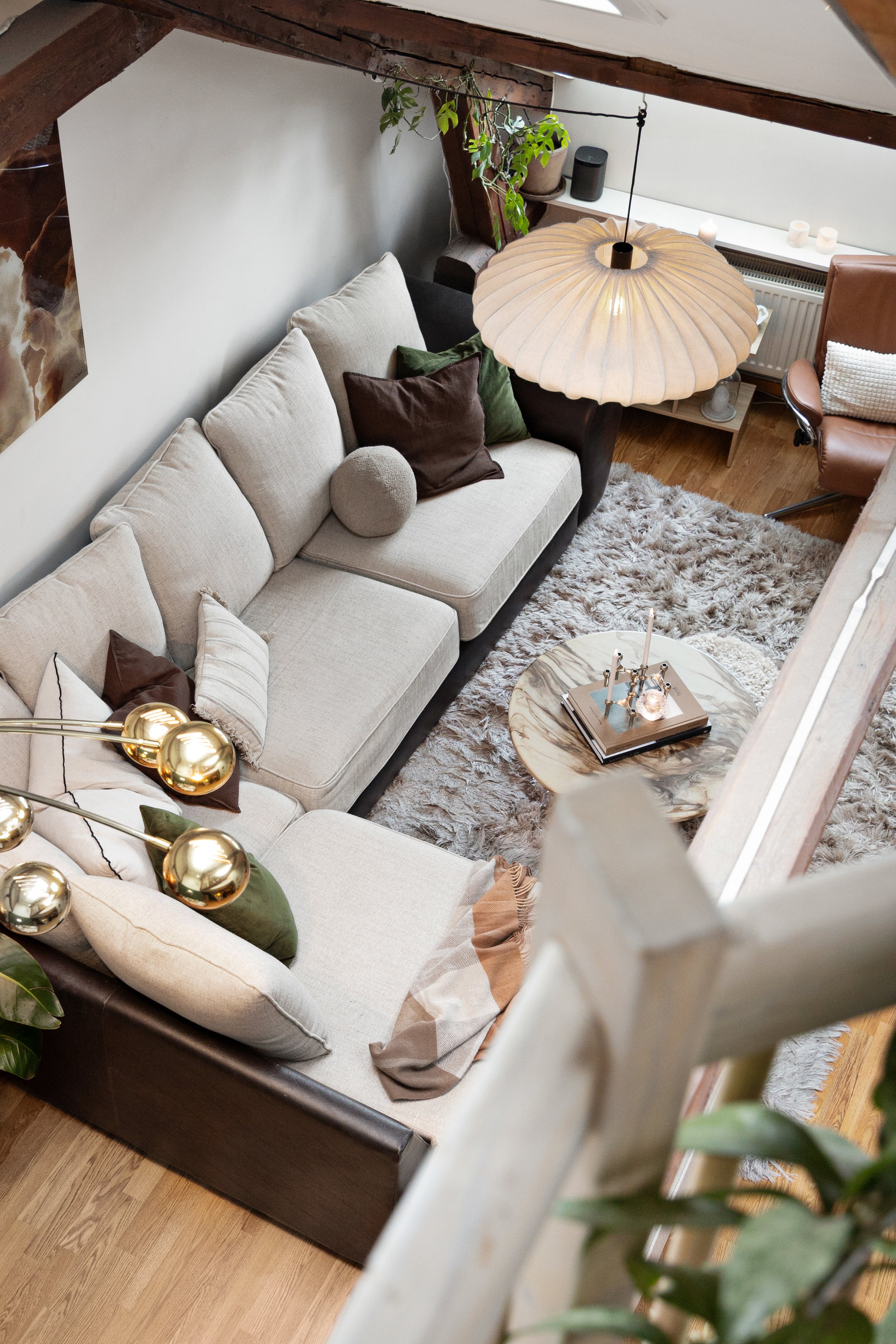 Bild av en lun stue med sofa, puter, teppe, et rundt bord og innendørs planter, sett fra en høy vinkel.