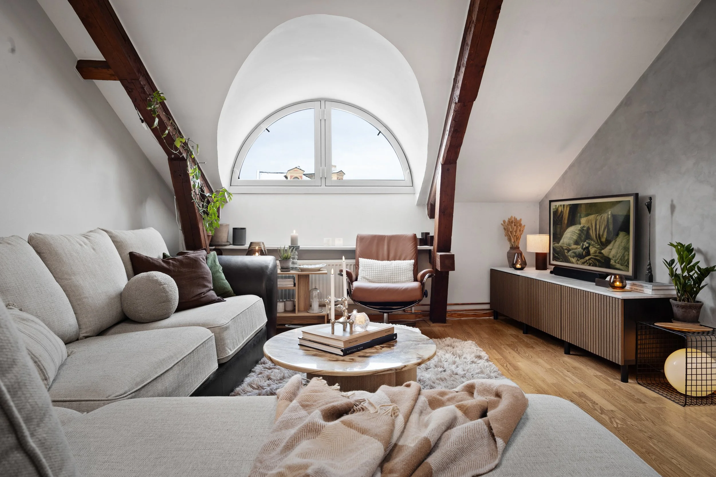 Stue med sofa, lenestol, TV, tre paneler, store vindusåpning, dragere og pyntedekorasjoner. Moderne og skandinavisk interiør.