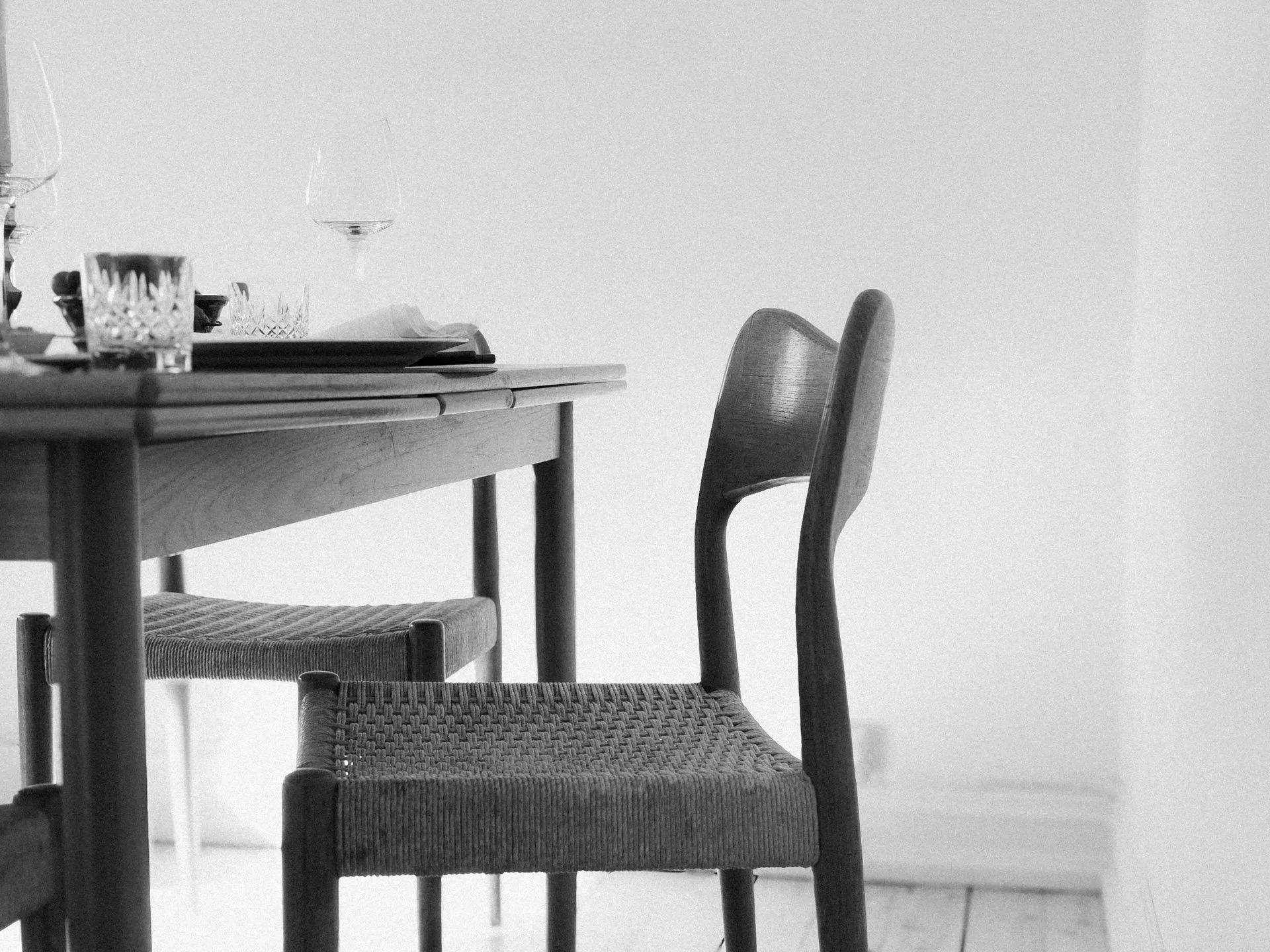 Et spisestuebord av tre med et glass og tallerkener, omgitt av danske designstoler, i et rom med hvite vegger.