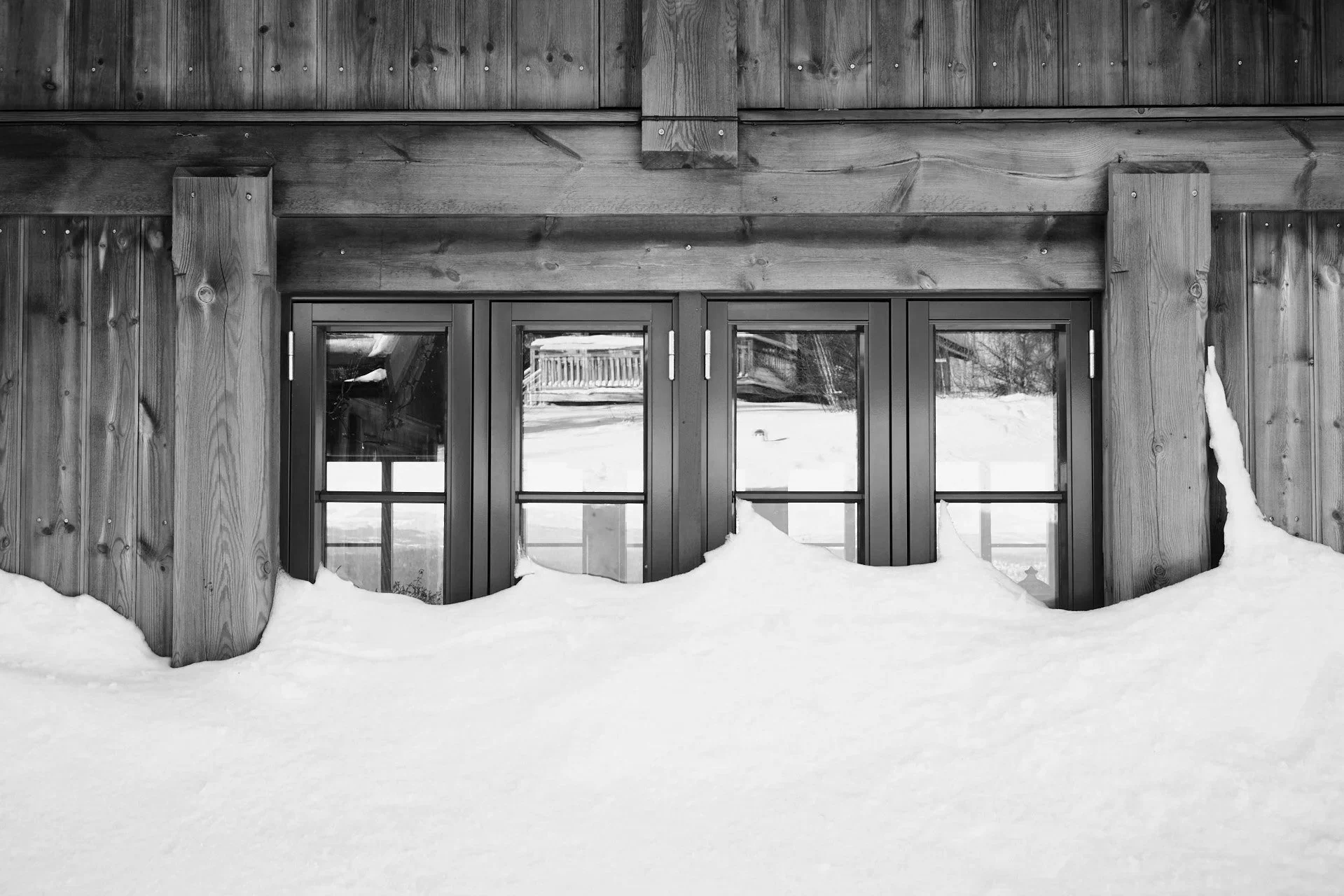 Et vindu i en tømmerhytte dekket av snø. Svart-hvitt bilde.