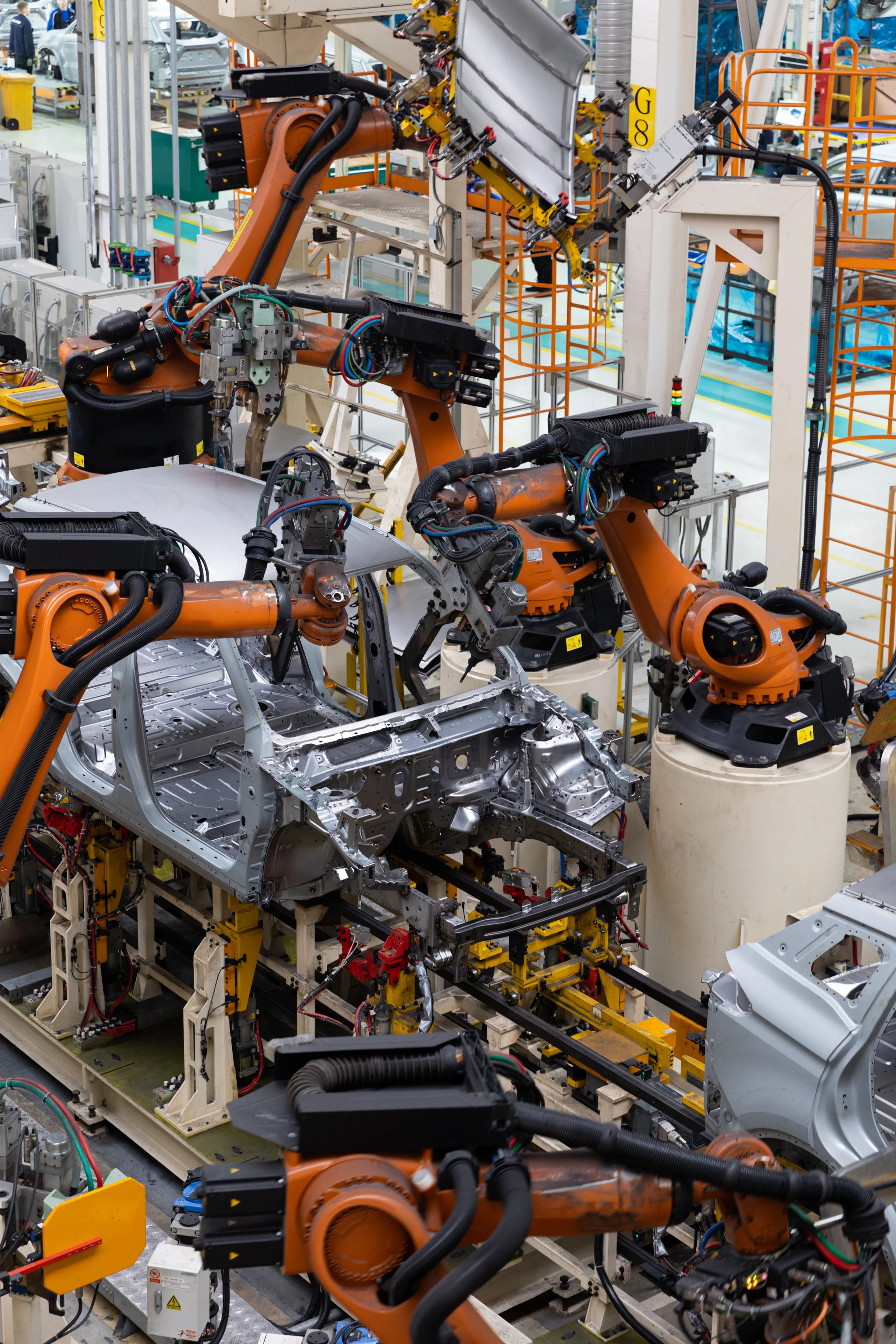 Industrial robotic arms assembling a car body on a production line in an automotive manufacturing plant.