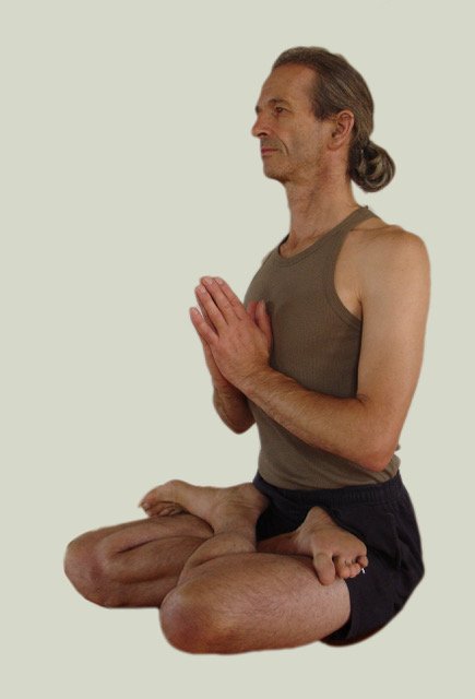 A man yoga practicing in a seated lotus position with hands in prayer pose
