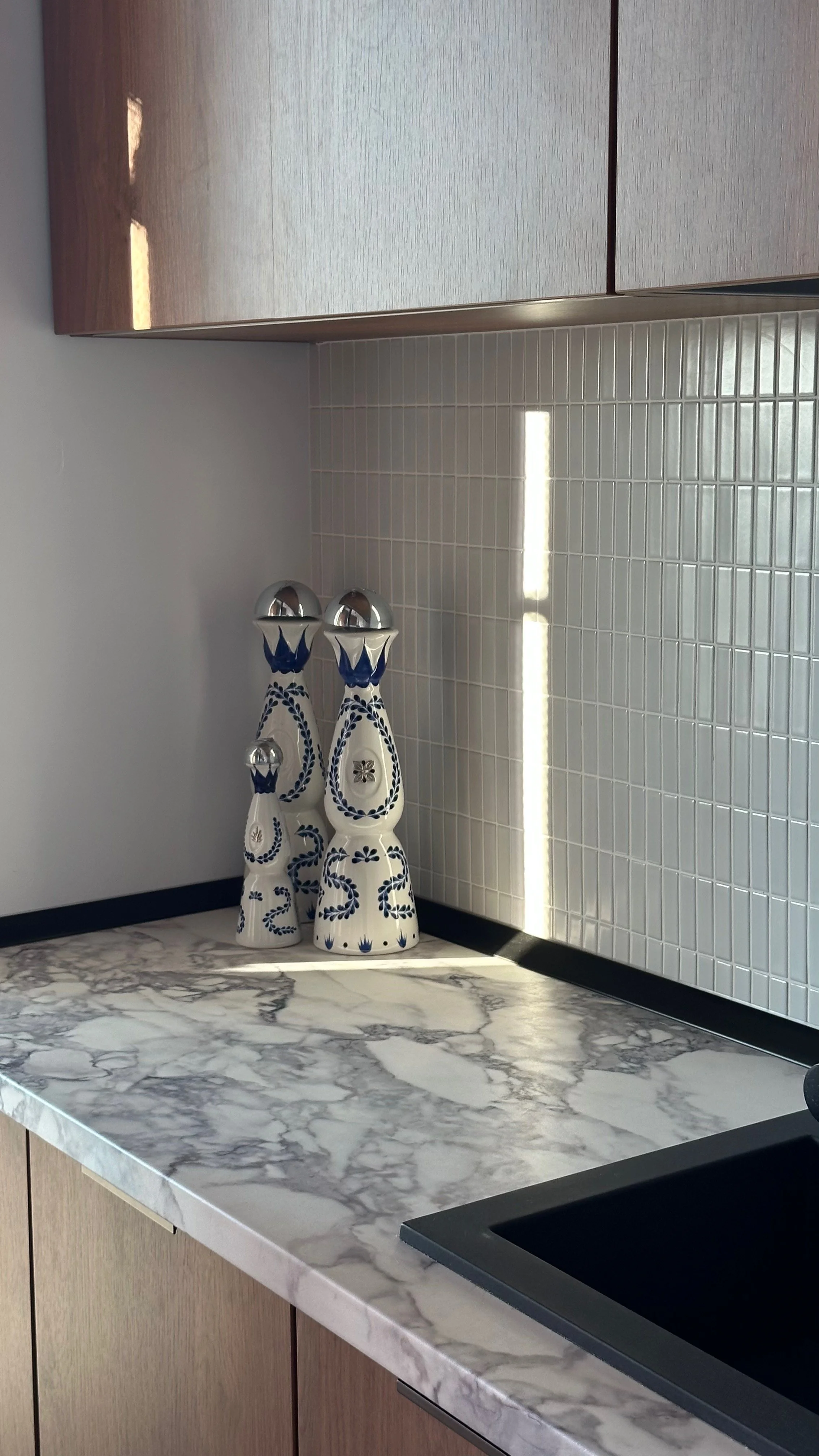 Decorative ceramic figurines with blue floral patterns on a marble countertop, against a tiled kitchen backsplash and upper wooden cabinets.