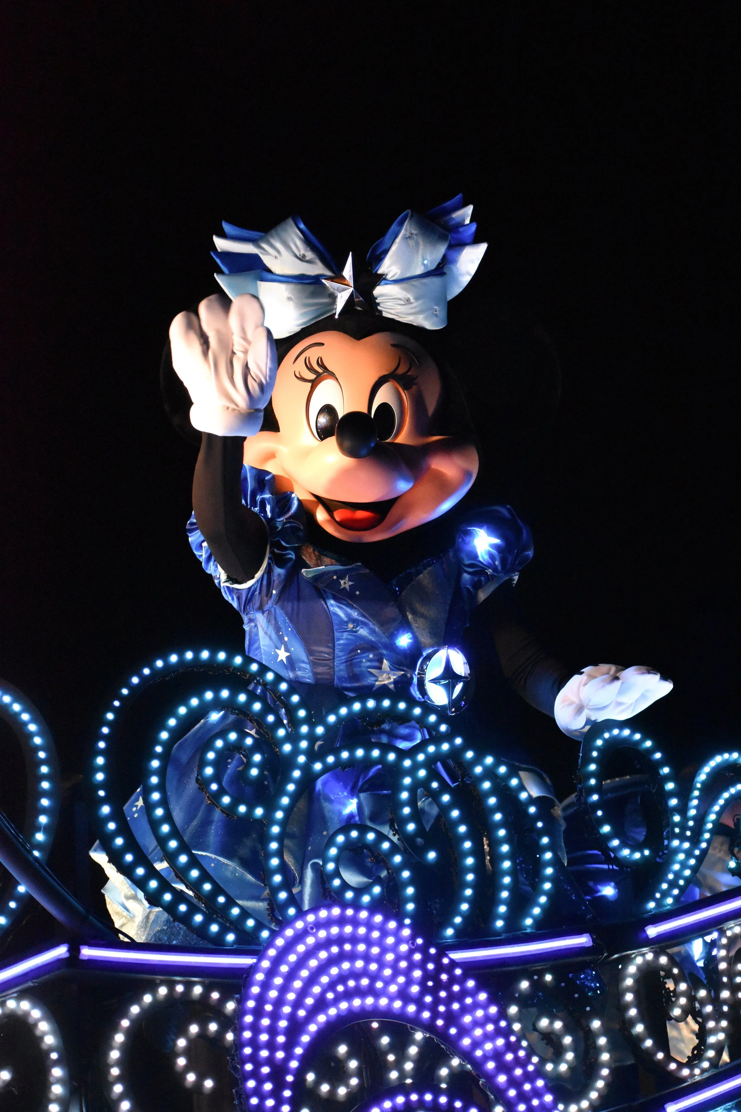Minnie Mouse costume decorated with lights at a nighttime parade or event.