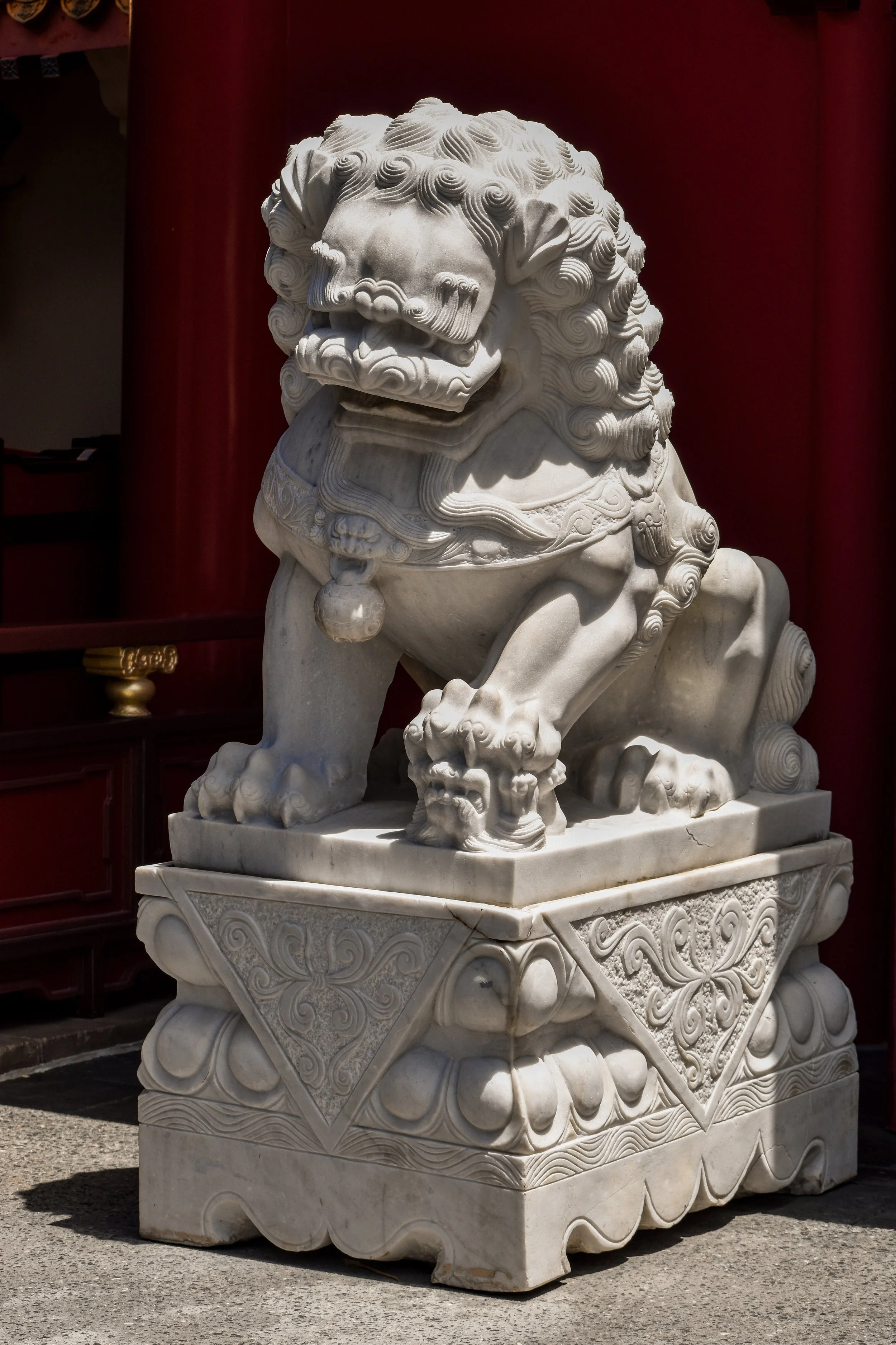 A carved white marble Chinese guardian lion statue, also known as a fu lion or foo dog, with detailed mane and features, placed on an ornate stone base.