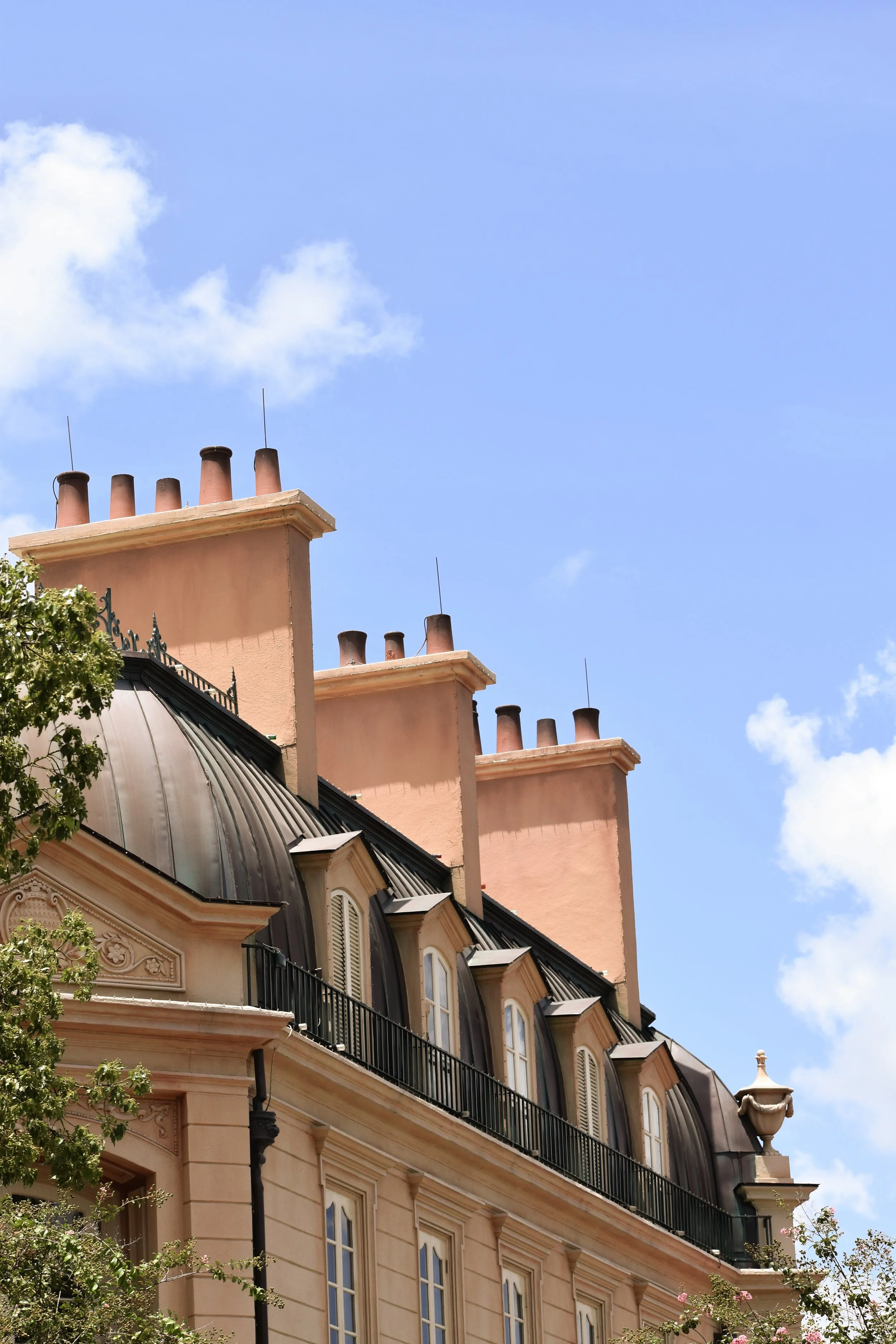 Upper part of a historic building with dormer windows and multiple chimneys on a blue sky with a few clouds.