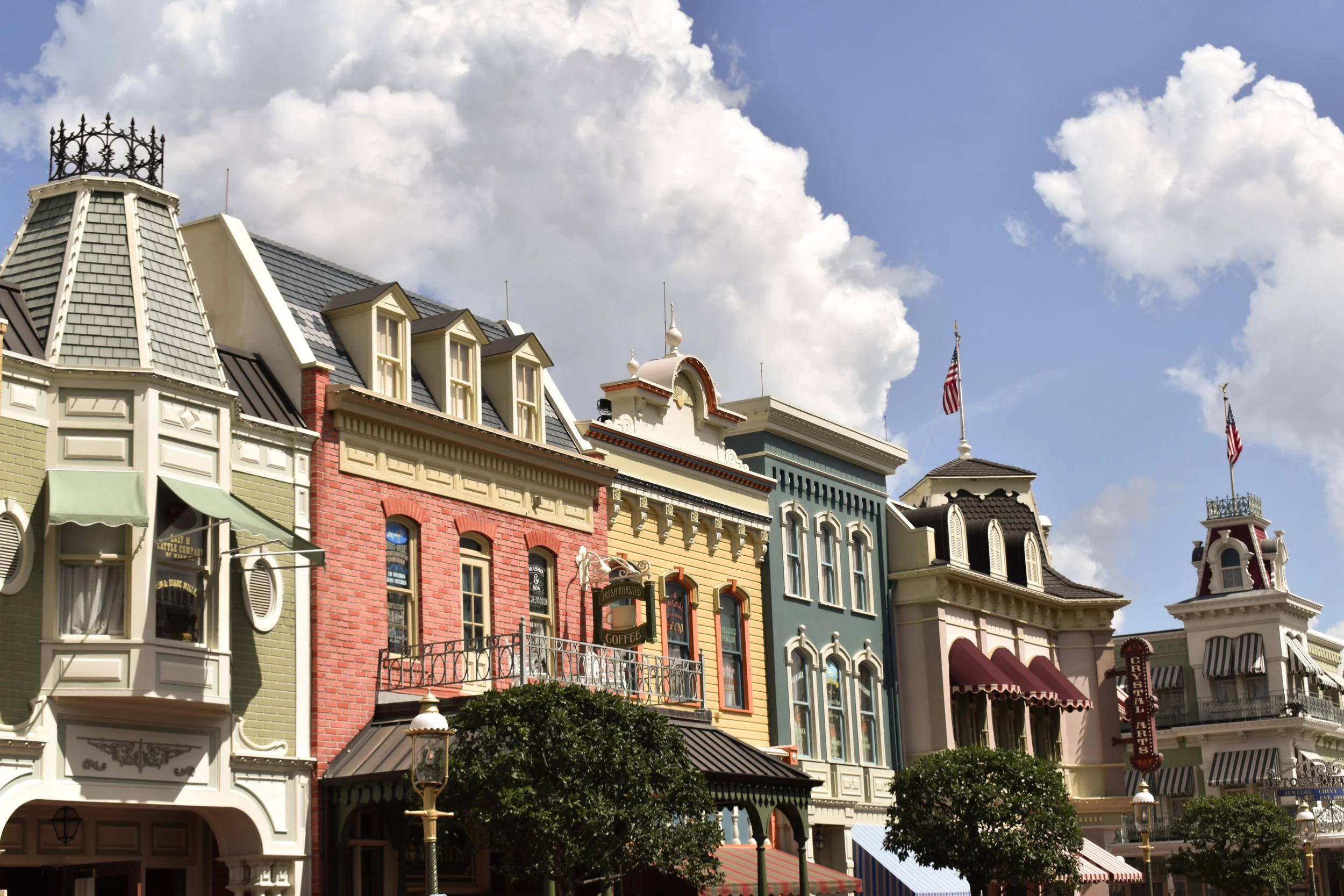Colorful Victorian-style buildings with American flags on rooftops and striped awnings, under a partly cloudy sky.