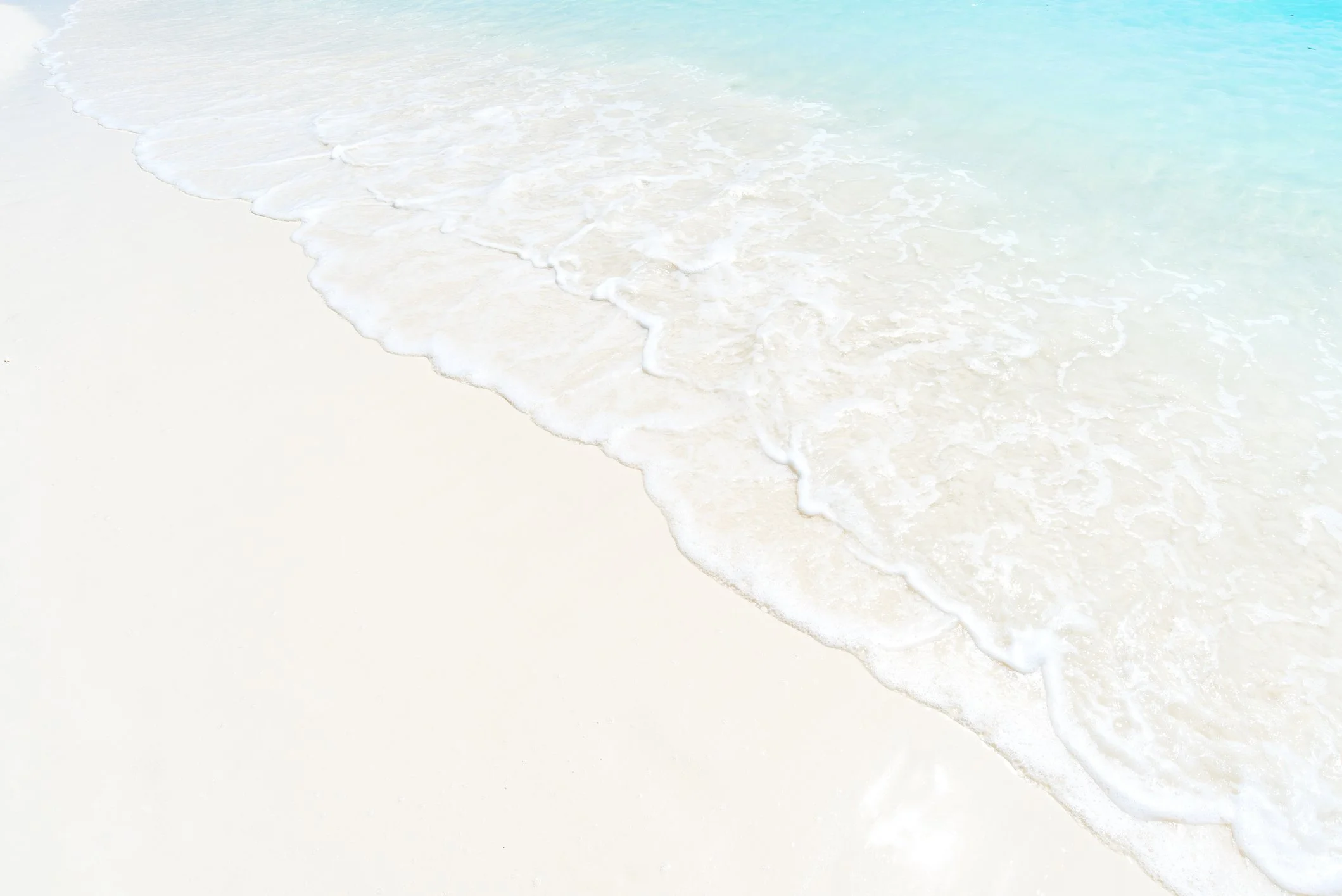 Gentle waves washing onto a white sandy beach.