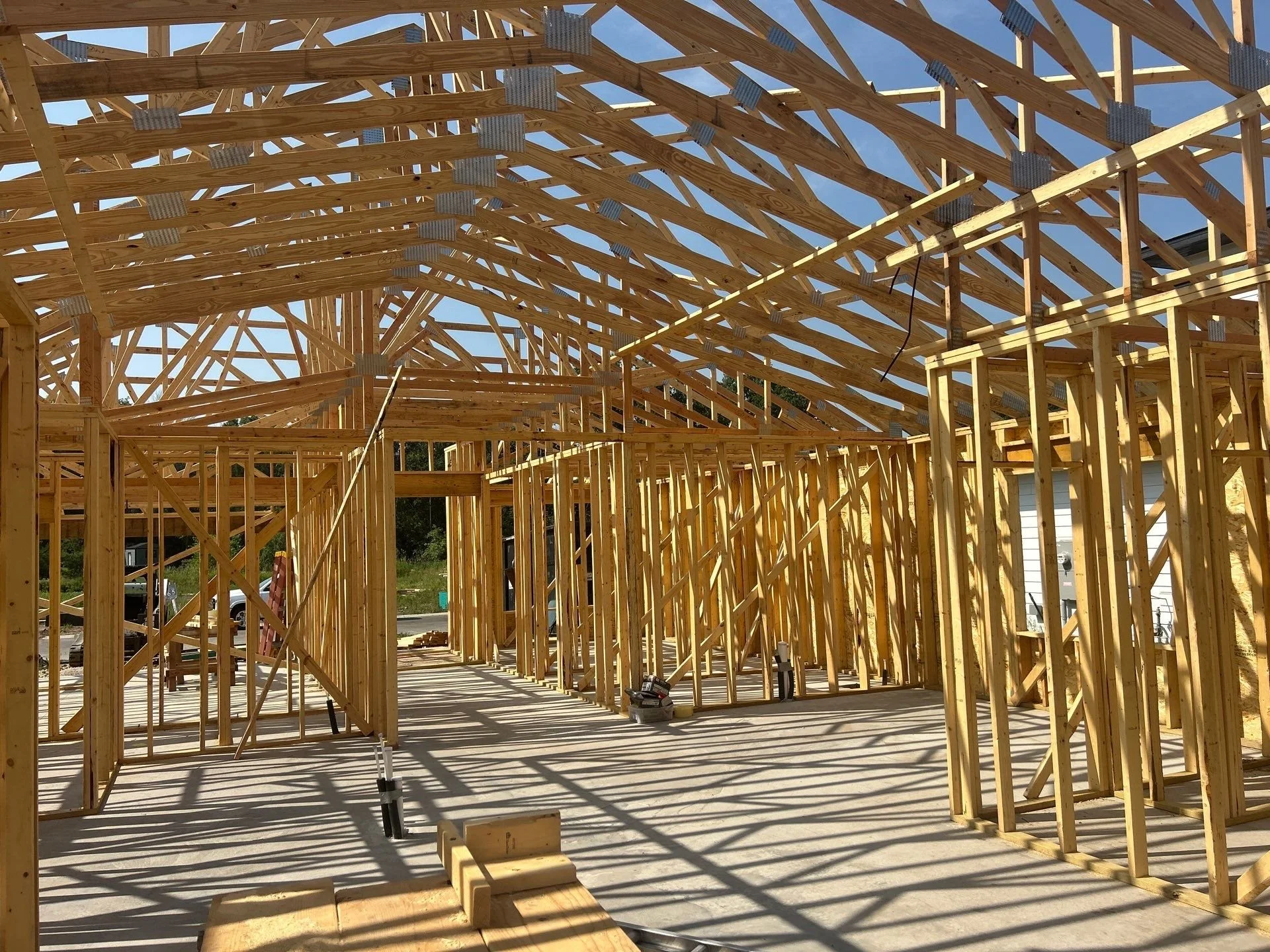 A construction worker in a yellow helmet and safety vest working on a wooden framework of a building against a blue sky.