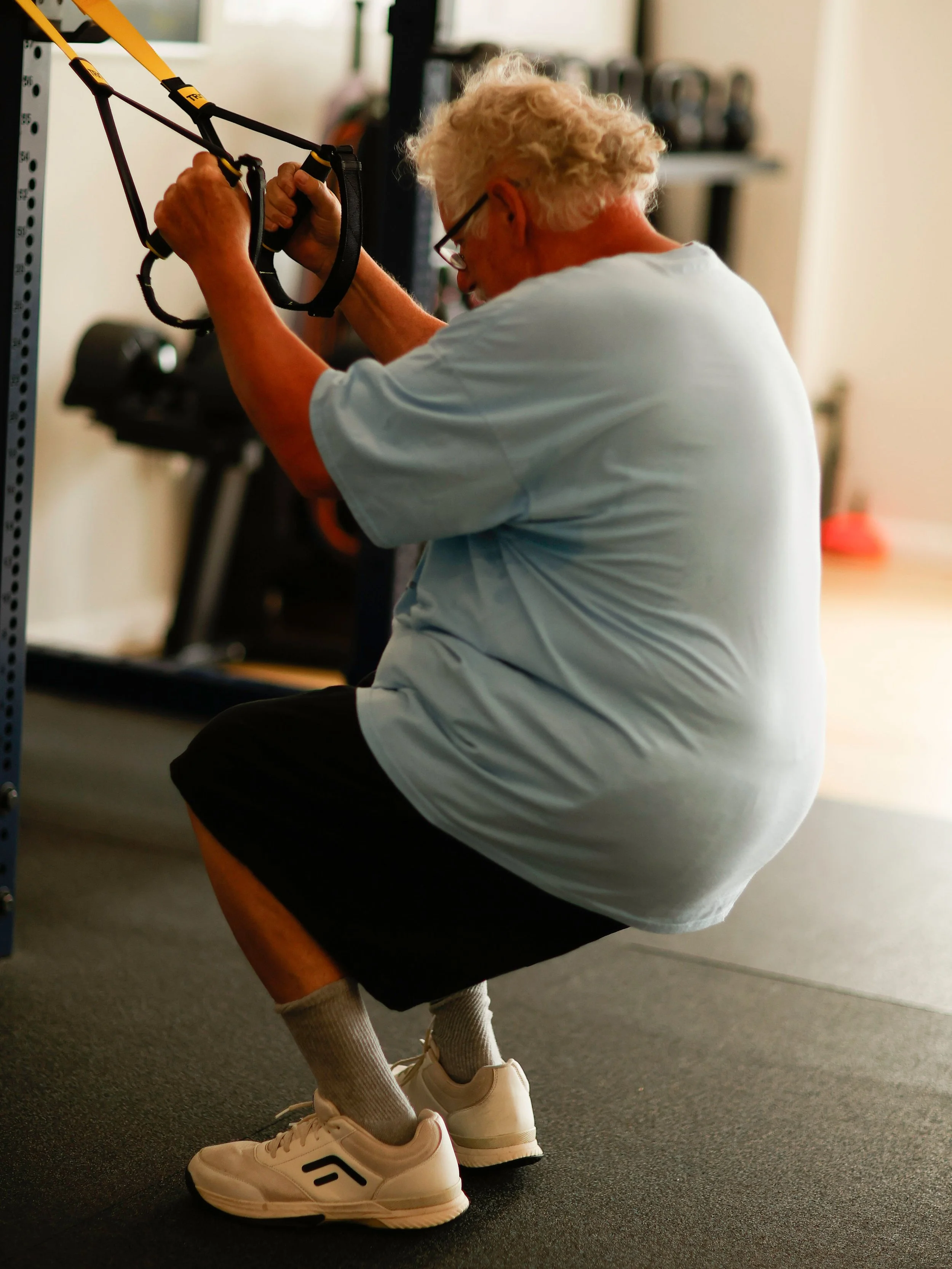 older adult doing TRX assisted squats during semi-private Training.