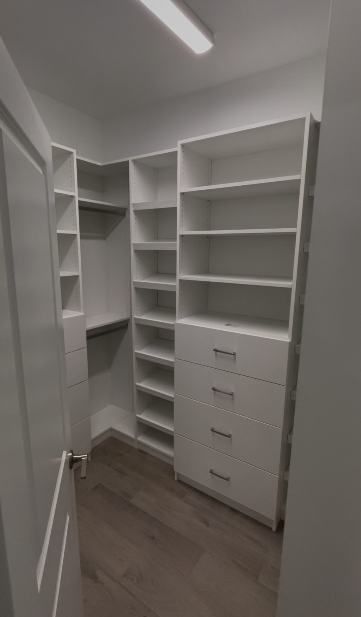 Empty white walk-in closet with built-in shelves, drawers, and a closet rod under a ceiling light.