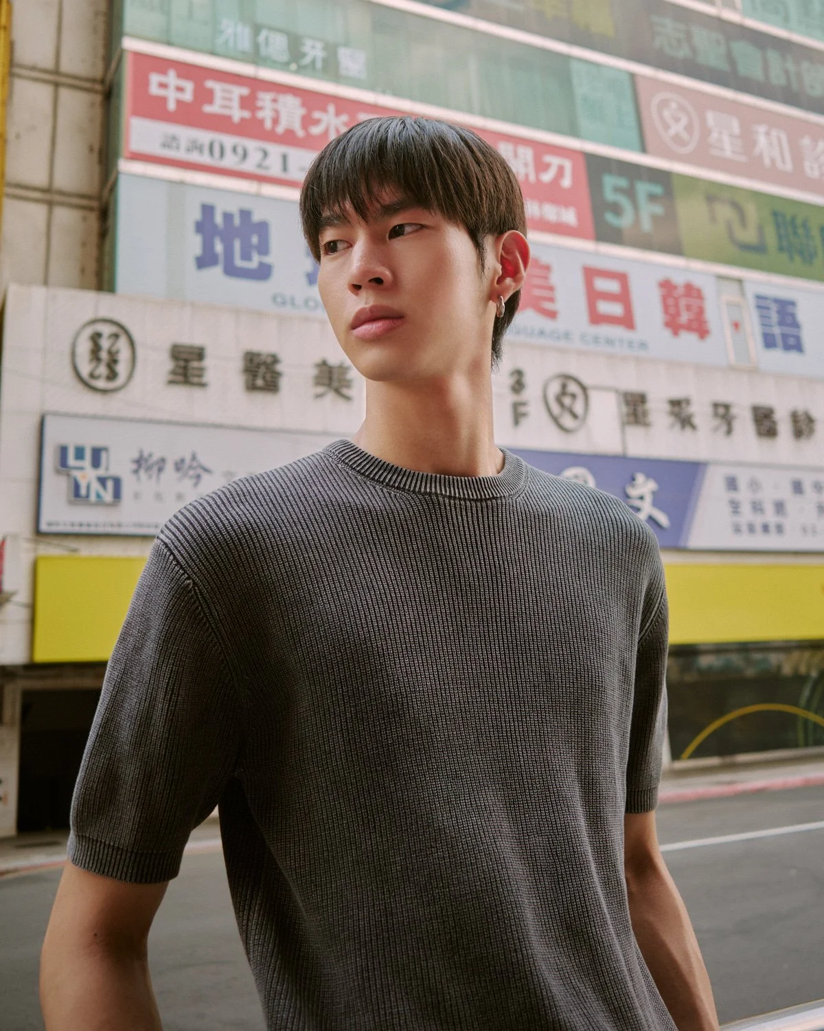 Male model in a grey knit top photographed in front of Taipei city signs by Pedro Márnez