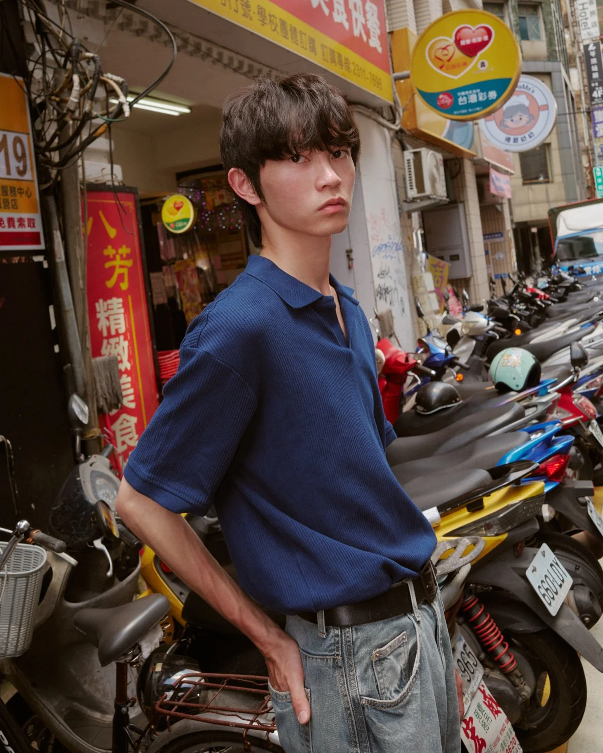 Male model in a blue polo shirt photographed among scooters and shops in Taipei by Pedro Márnez
