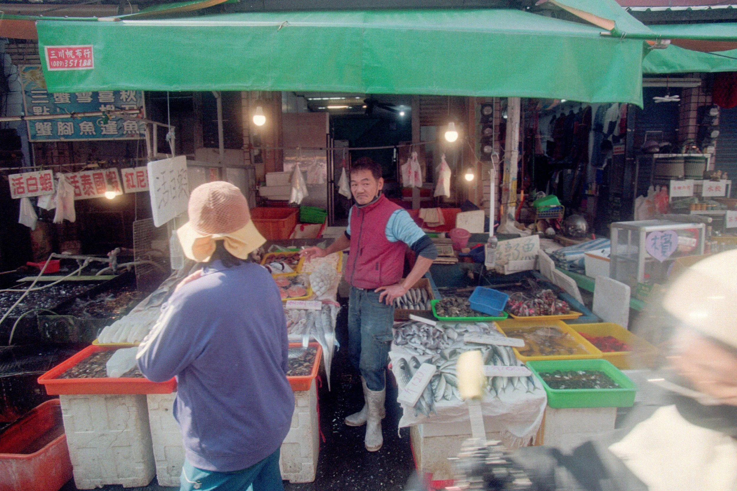 Vendeur de poissons dans un marché asiatique, avec des morceaux d'animaux marins exposés sur une table.